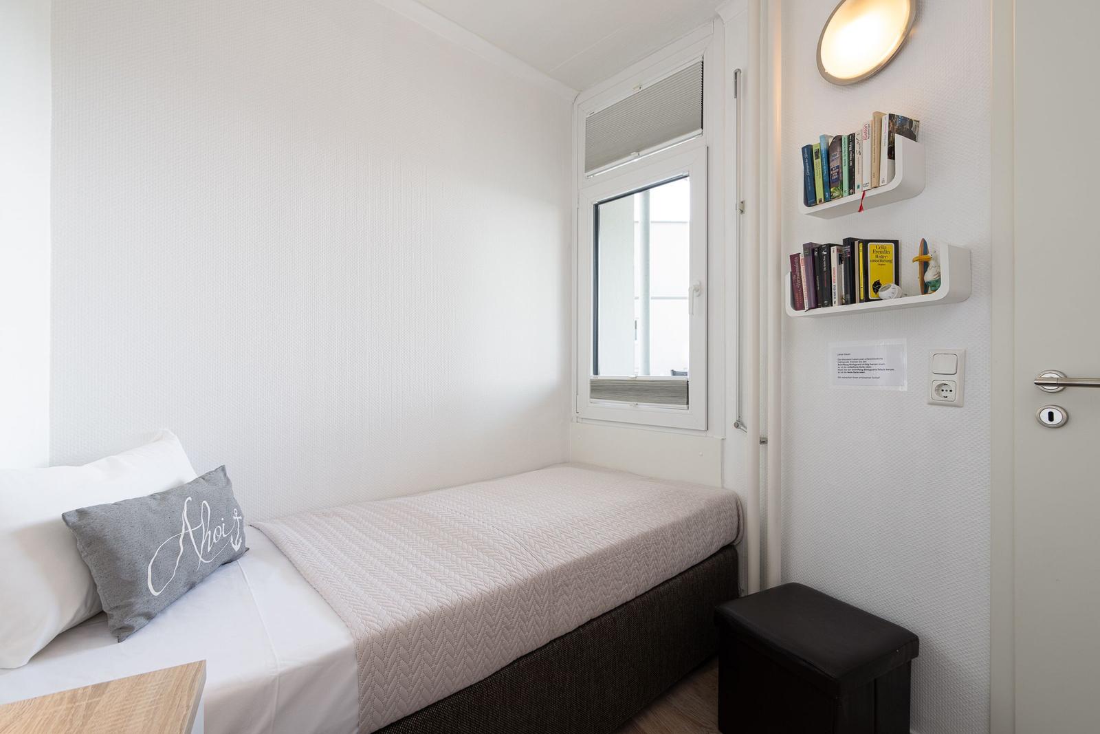 Ein Schlafzimmer mit Bett, Fenster und Wandregalen mit Büchern.