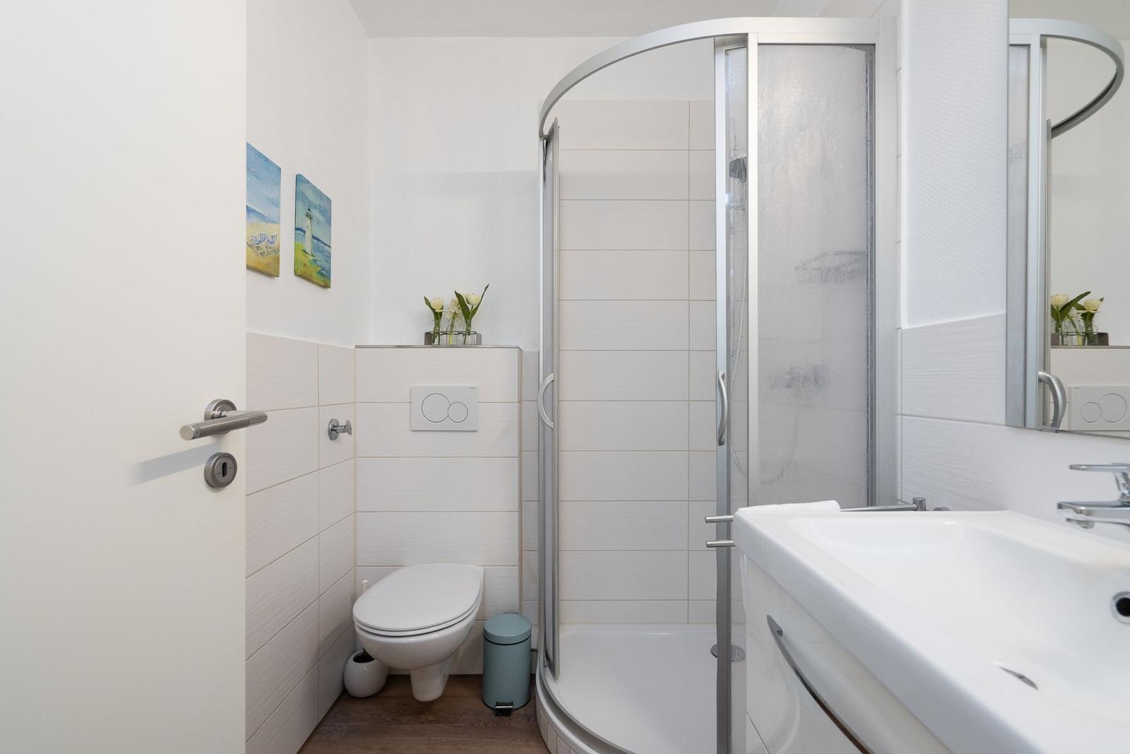 Badezimmer mit Dusche, Waschbecken und Toilette. Wandgestaltung mit Bildern.