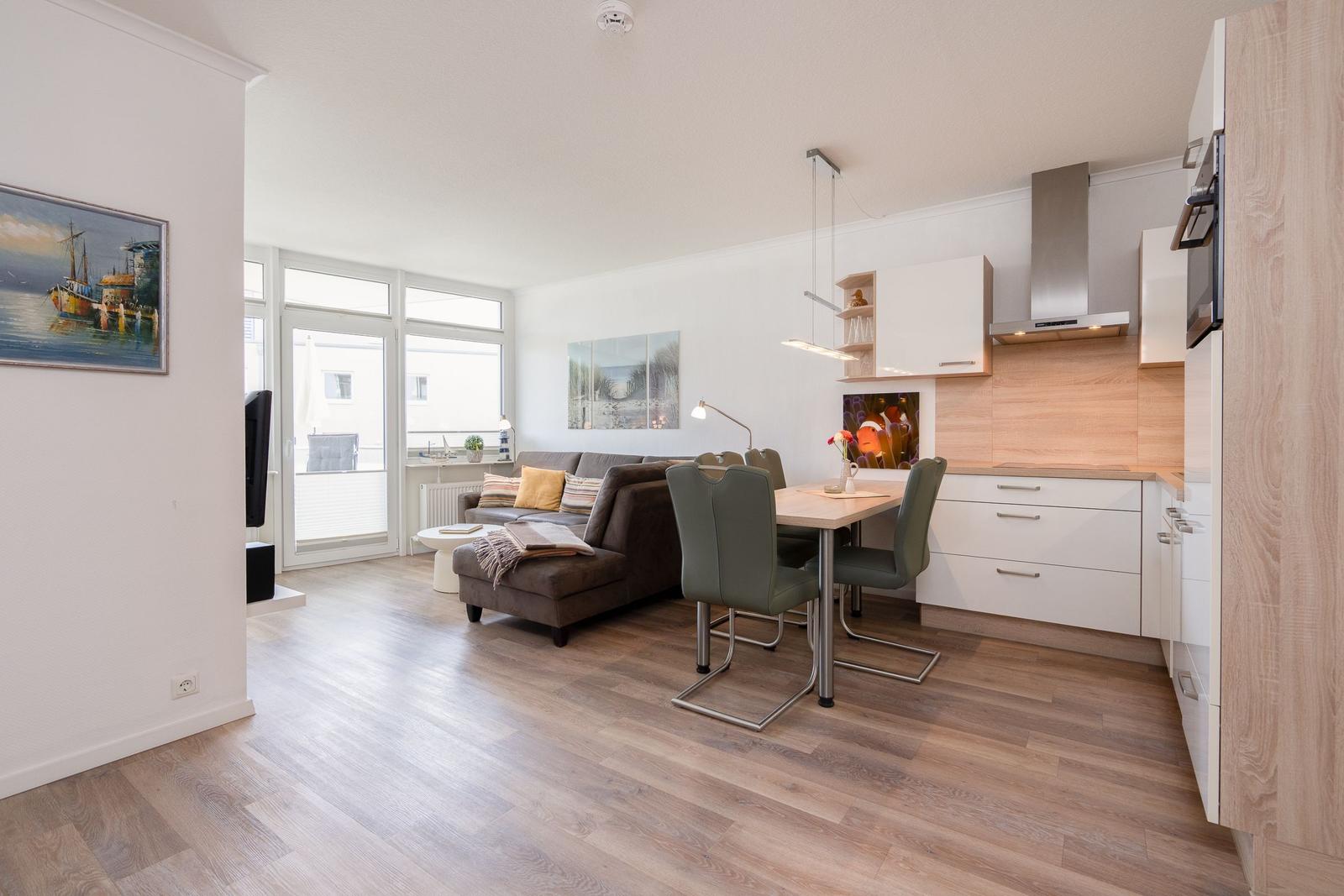 Wohnküche mit Esstisch, Sofa und Holzboden. Fenster zur Terrasse.