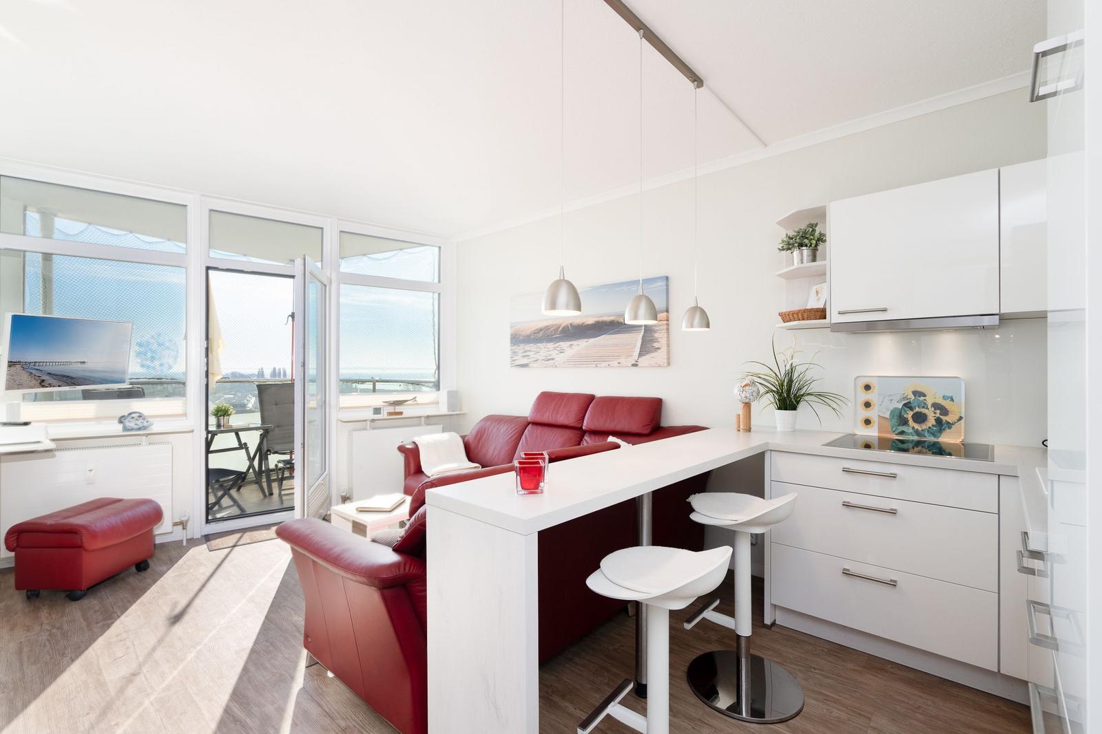 Living area with red sofa, white kitchen units, and view of balcony.