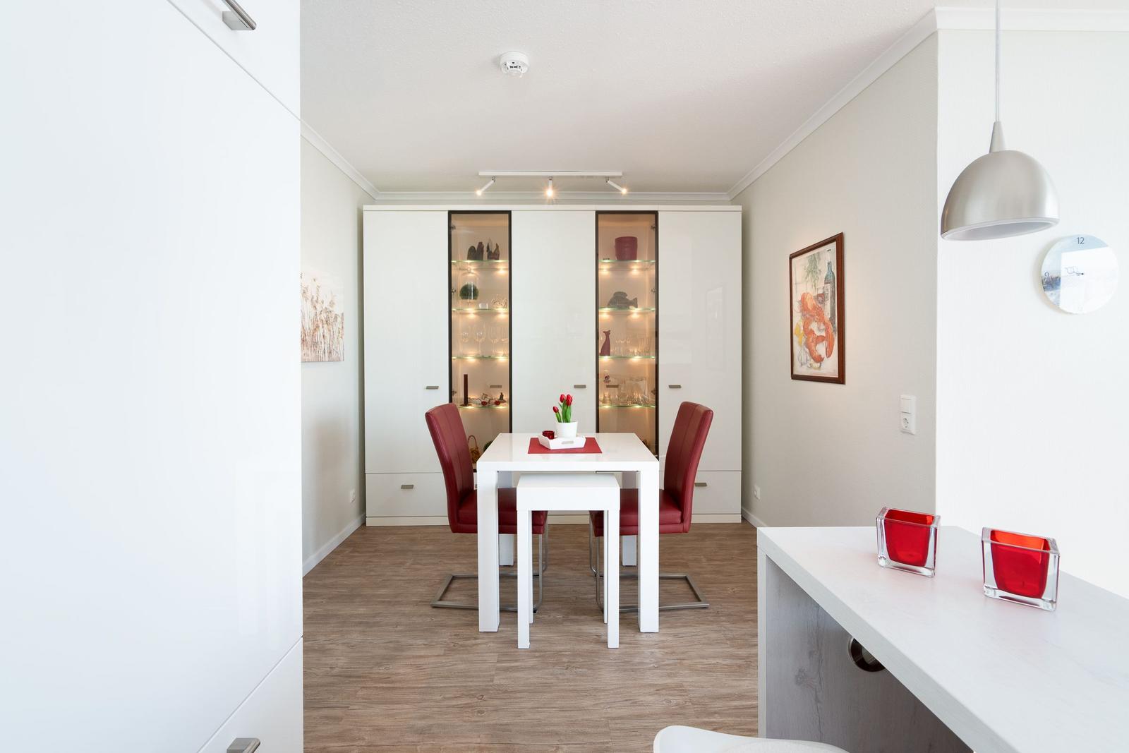 Dining room with white table, red chairs, and glass cabinets. Wooden floor and pendant lamp.