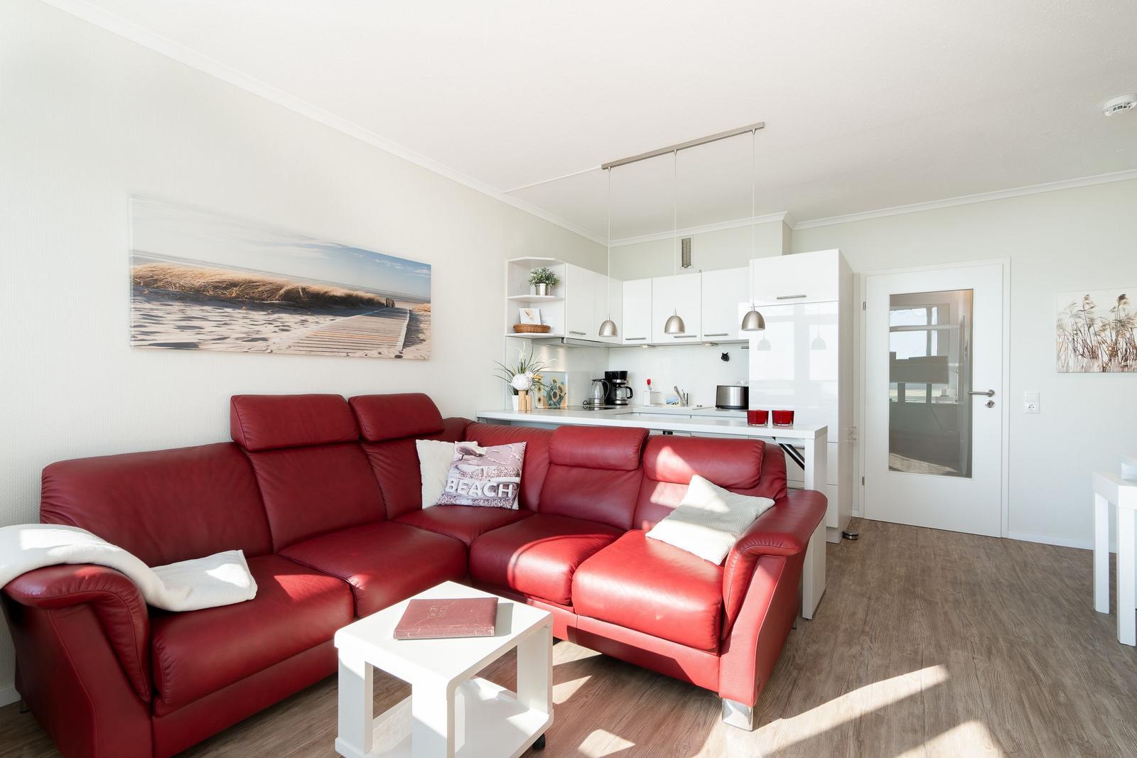 Red leather sofa in living area with kitchenette and wooden floor.