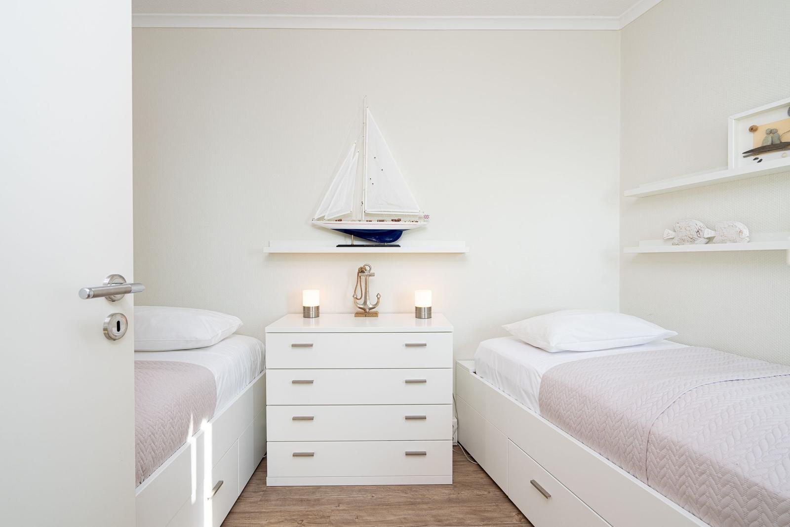 Two single beds flank a white dresser with sailboat model and lantern.