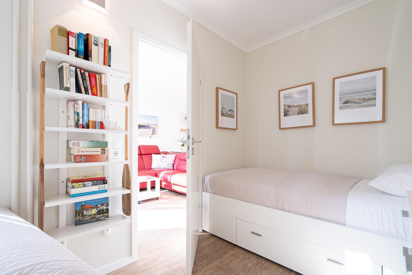 Bedroom with bed and bookcase. Passage to living room with red sofa.