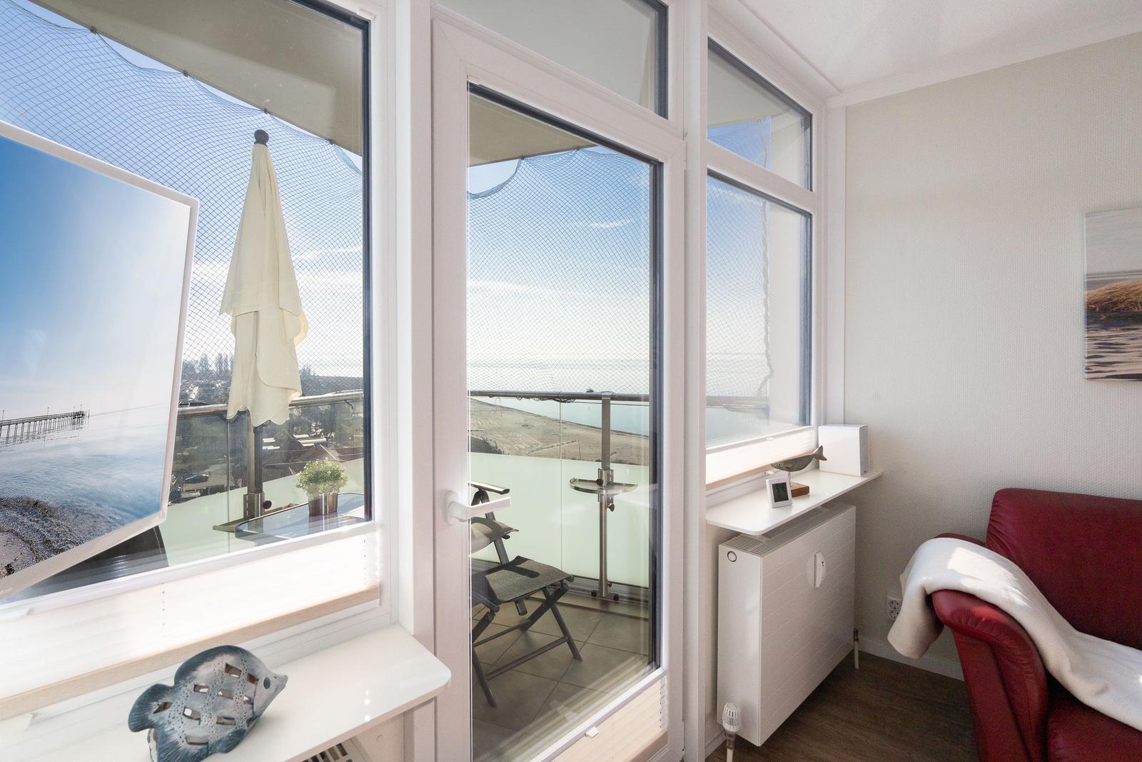Room with view of balcony and sea, red armchair and windows with net.