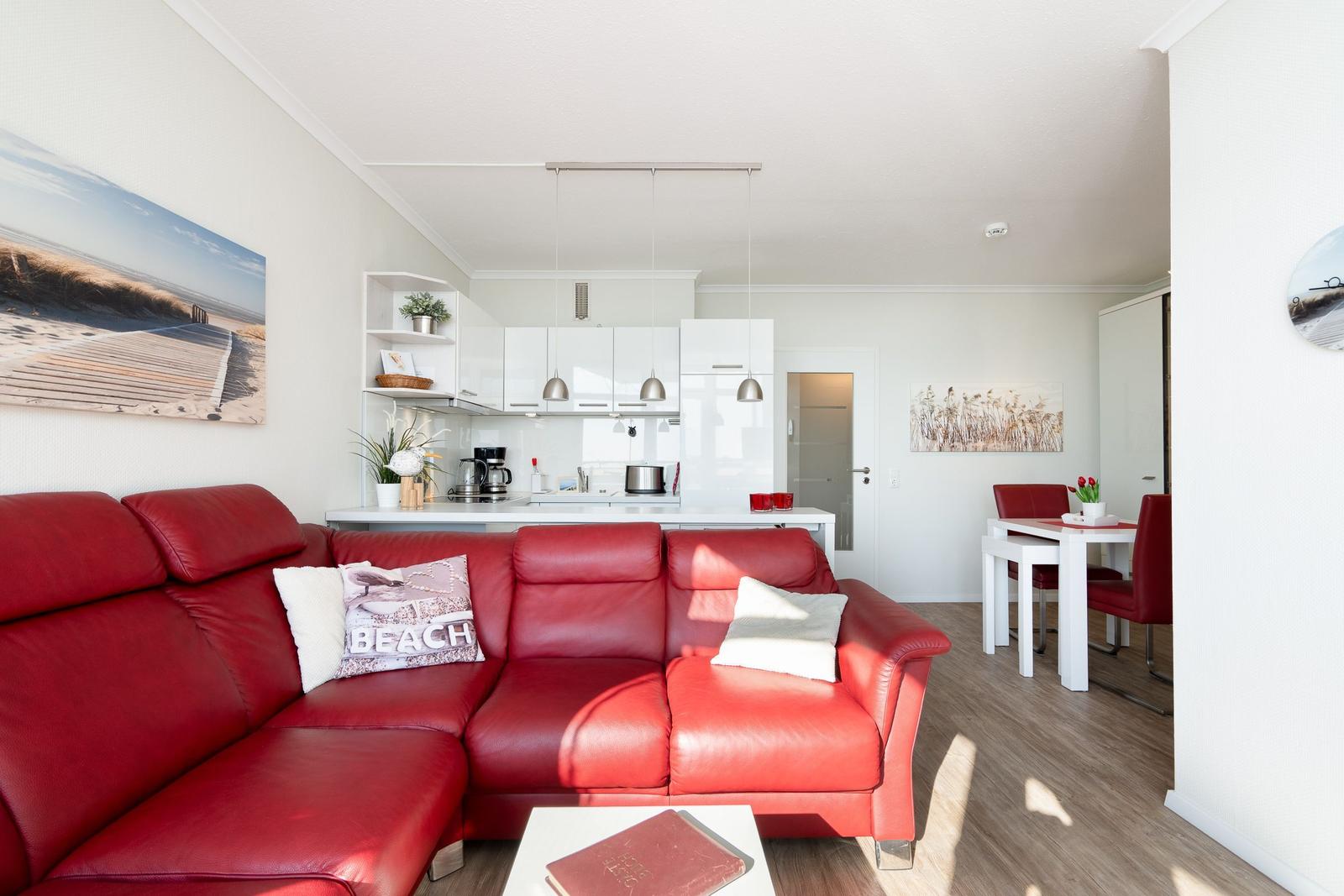 Living and dining area with red sofa, white kitchen, and dining set.
