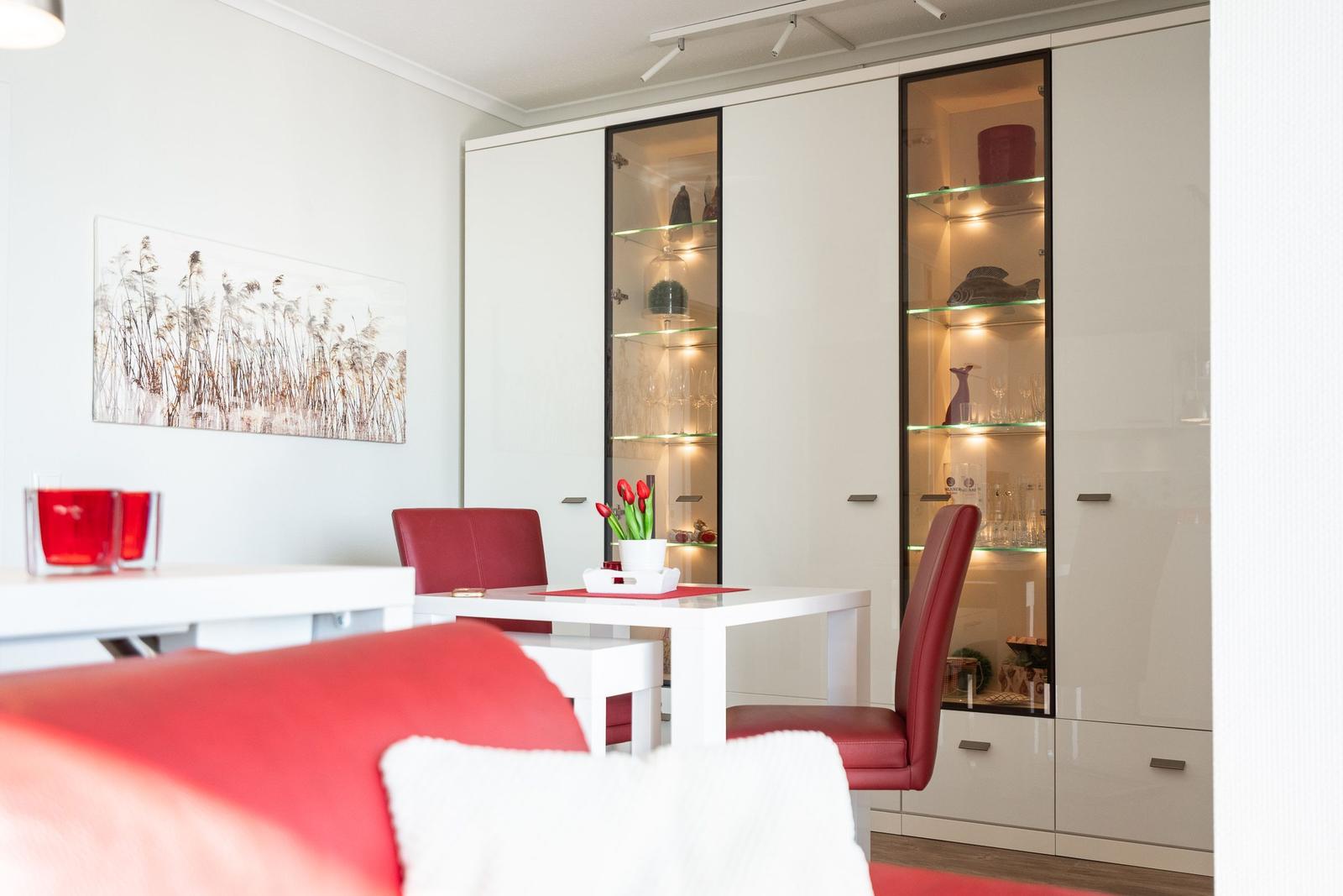 Dining area with white table, red chairs, and glass cabinets on the wall.