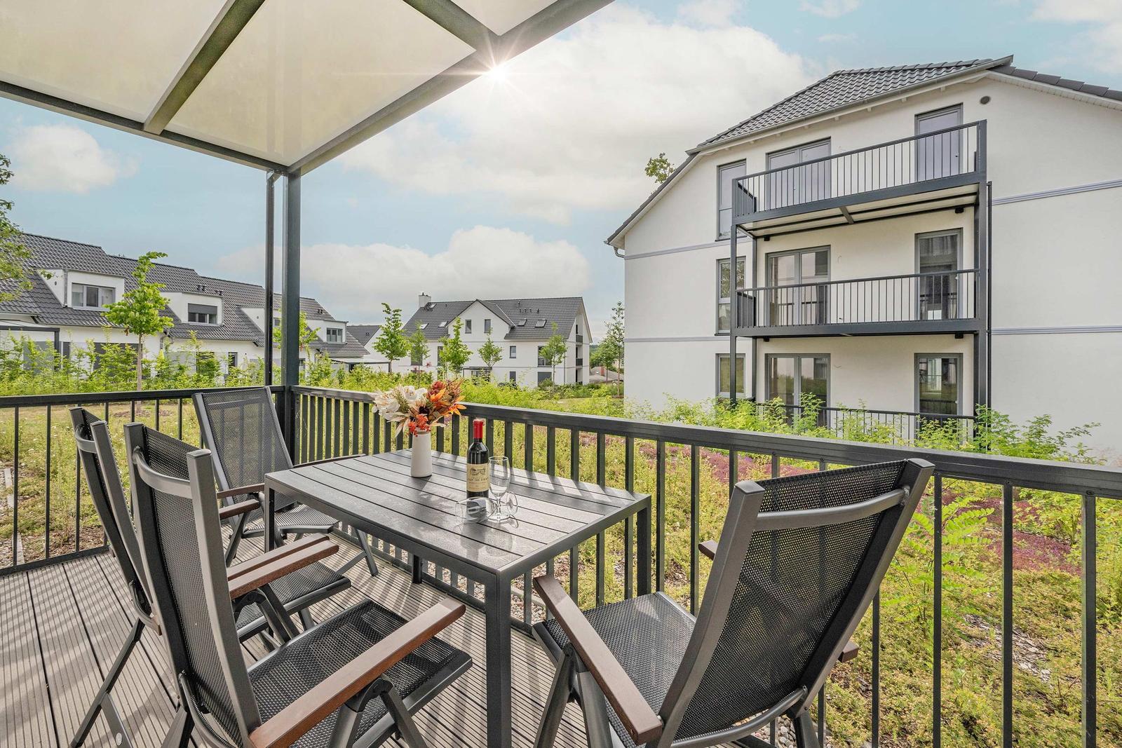 Terrasse mit Tisch, Stühlen und Wein. Blick auf moderne Häuser und Grünflächen.