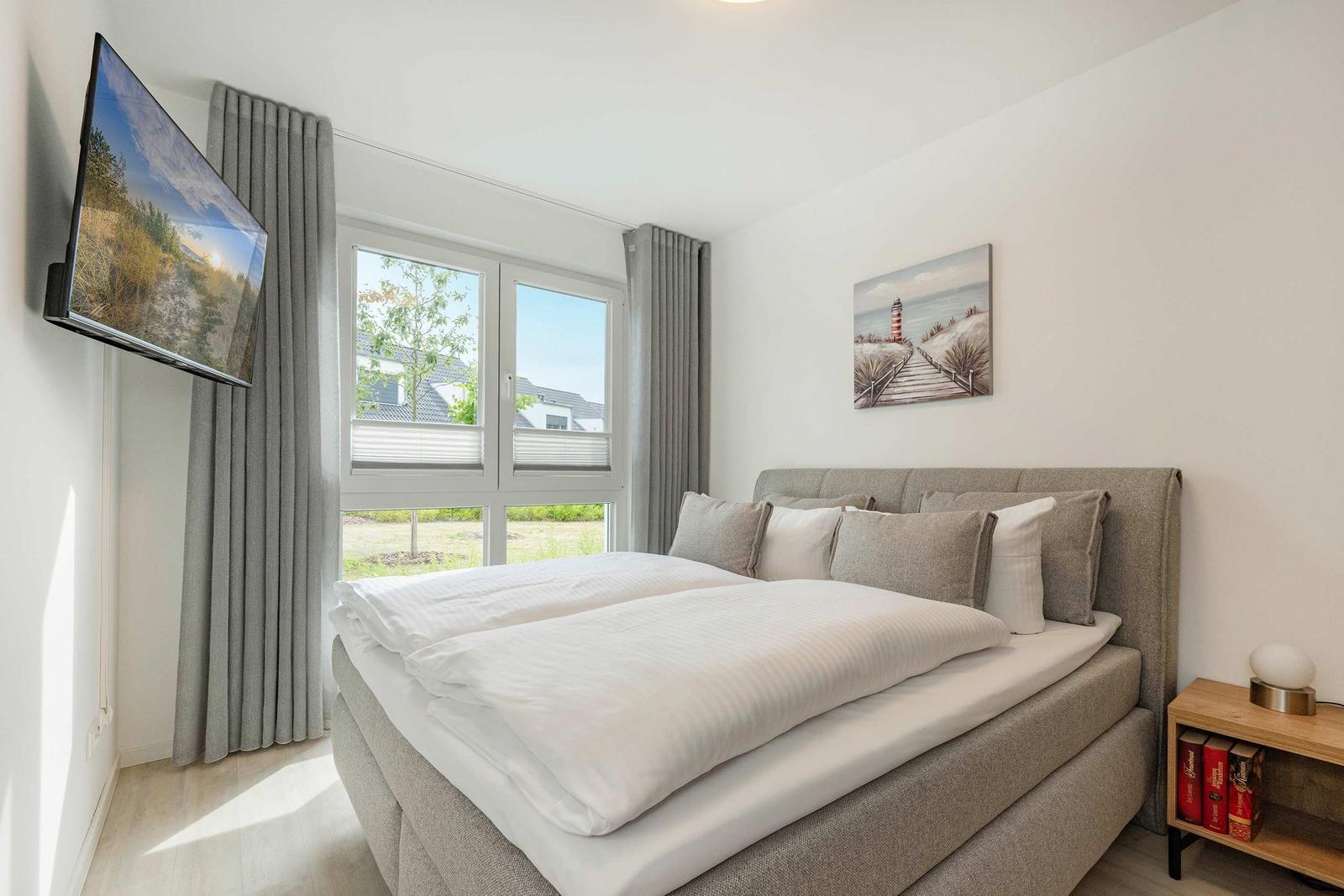 Schlafzimmer mit Bett, Fenster und Wandbild. TV an der Wand.