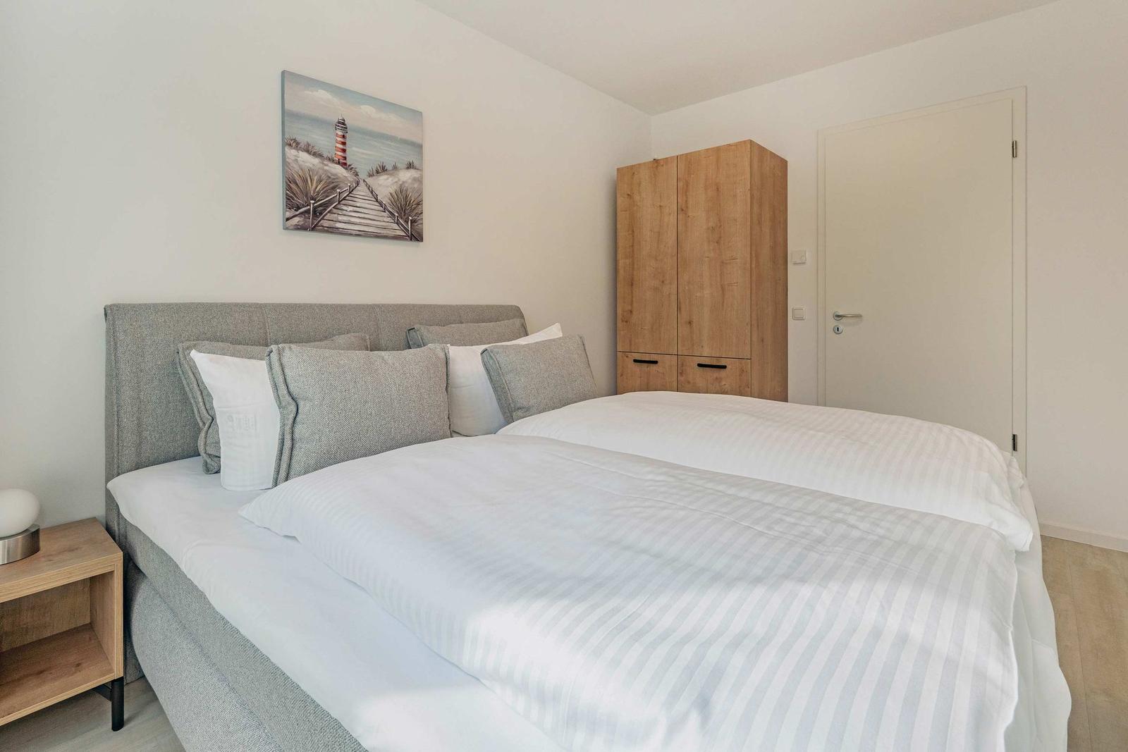 Schlafzimmer mit Doppelbett, Holzschrank und Wandbild mit Leuchtturm.