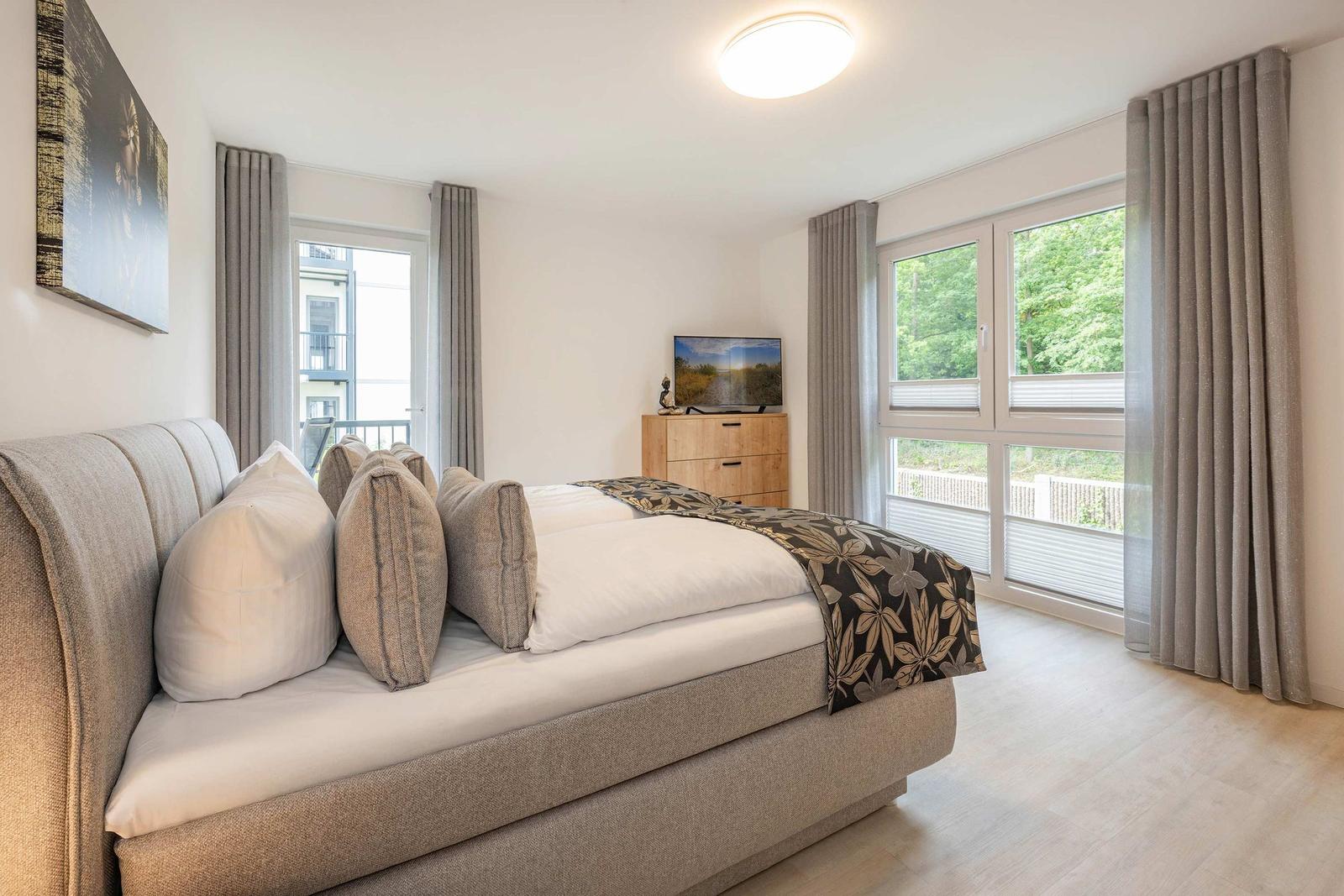 Schlafzimmer mit großem Bett, Fenstern und TV.