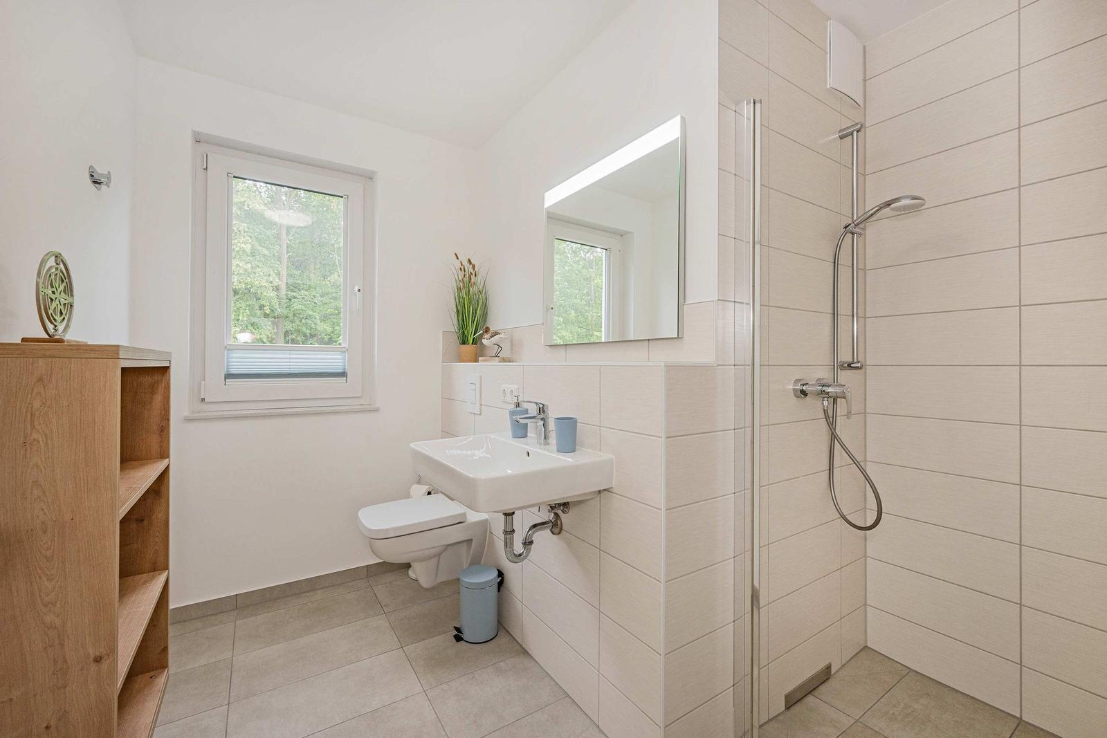 Badezimmer mit Dusche, Waschbecken und Toilette. Fenster mit Blick auf Grün.