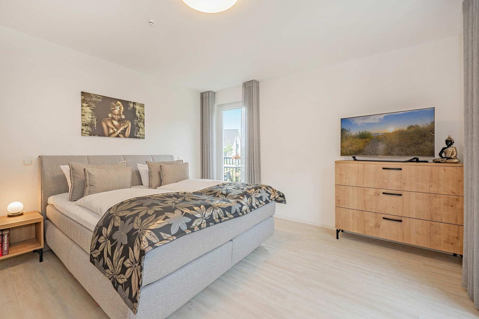 Schlafzimmer mit Bett, Fernseher und Fenster zur Terrasse.