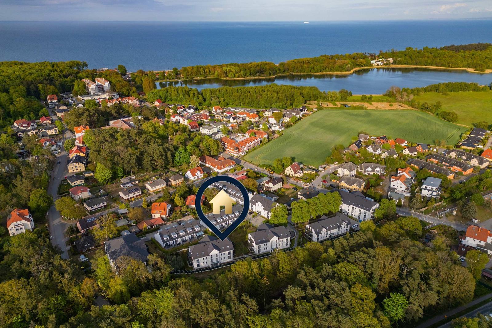 Luftbild von Ferienwohnungen in einer grünen Umgebung mit See und Meer im Hintergrund.