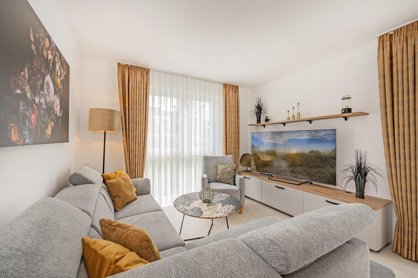 Wohnzimmer mit Sofa, Fernseher und großen Fenstern.