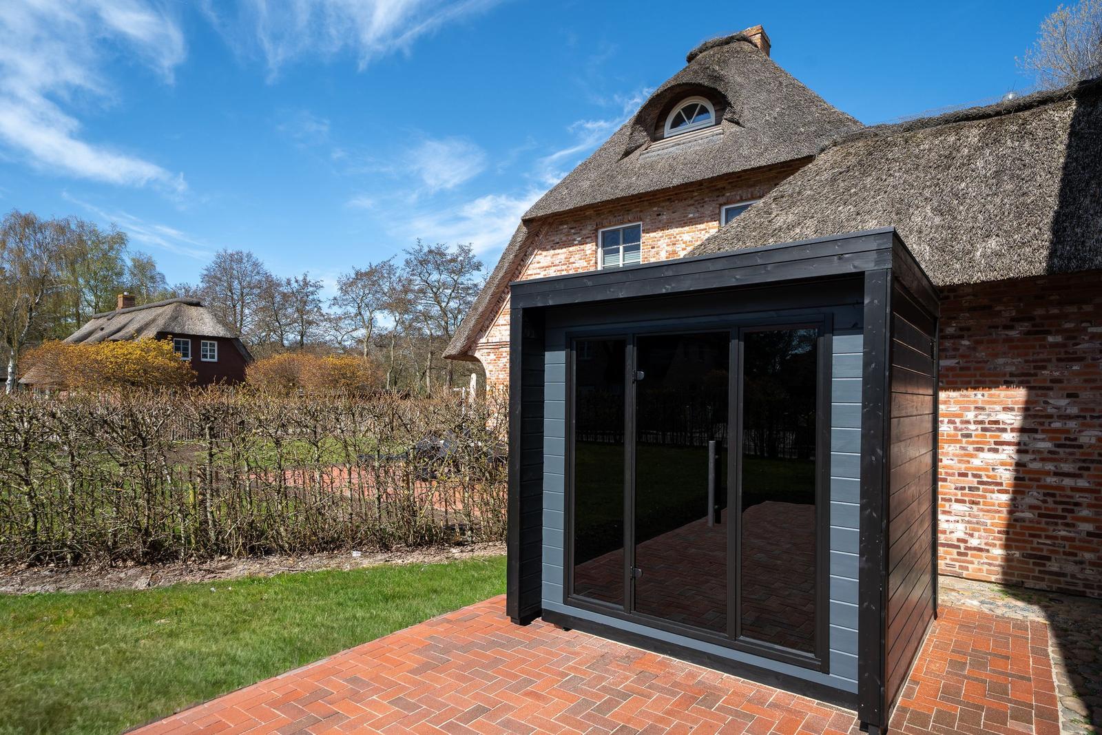 Moderne Terrasse mit Glas-Türen an traditioneller Strohhausbauweise.
