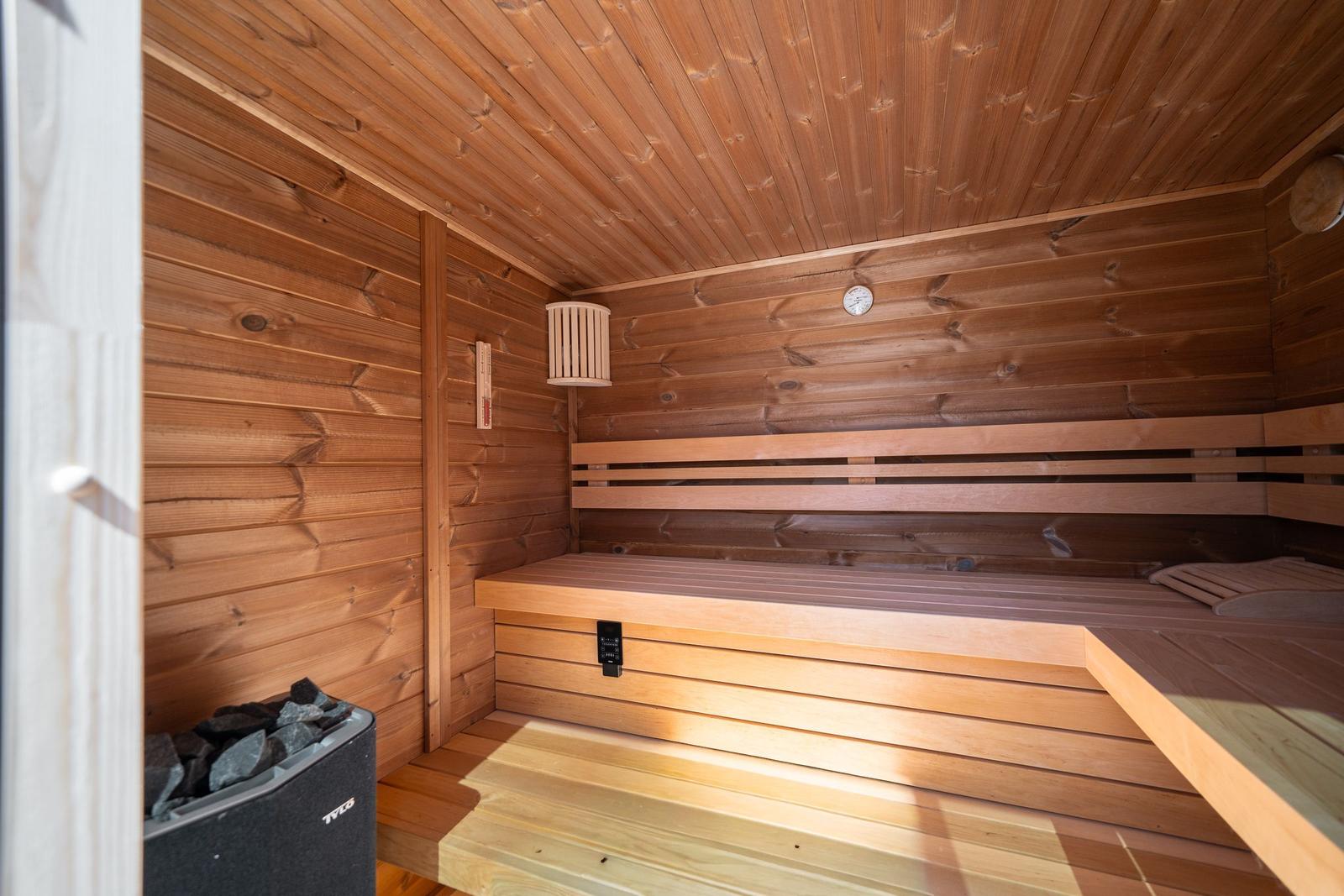 Sauna mit Holzbank und Thermostat. Steine im Ofen. Holzwände und -decke.