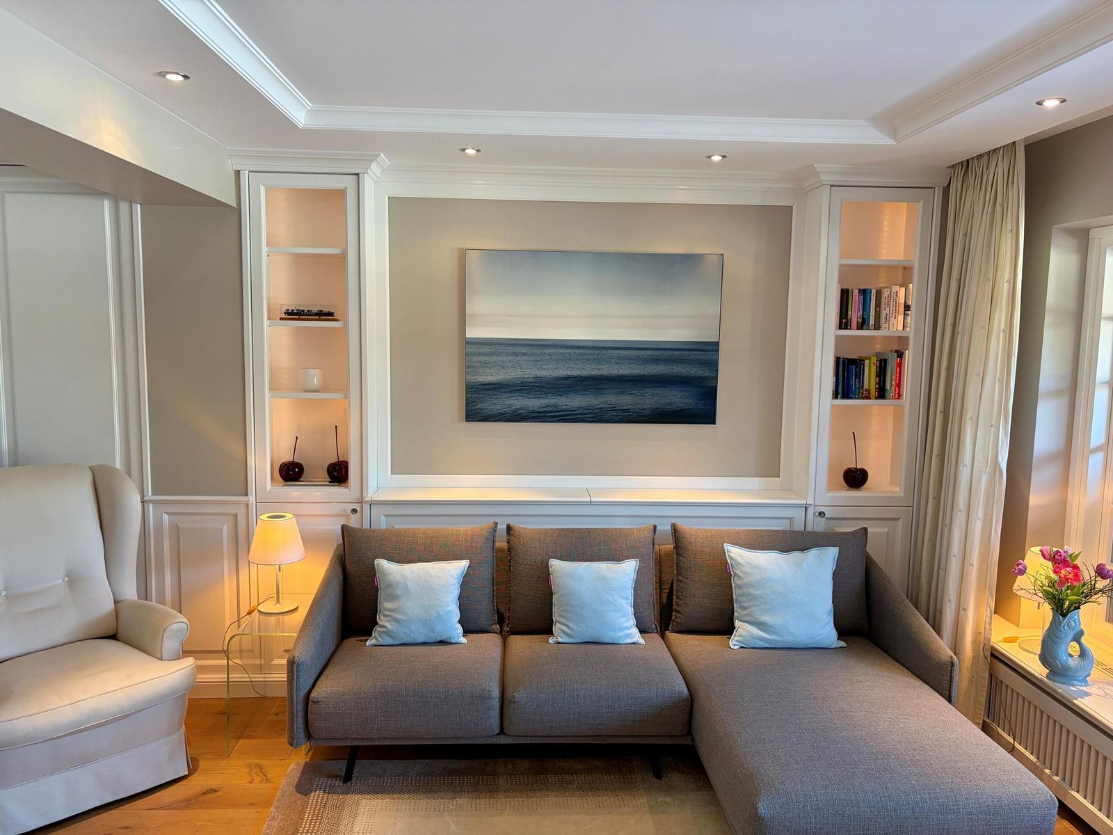 Wohnzimmer mit Sofa, Sessel und Wandbild. Regale mit Büchern und Dekoration.
