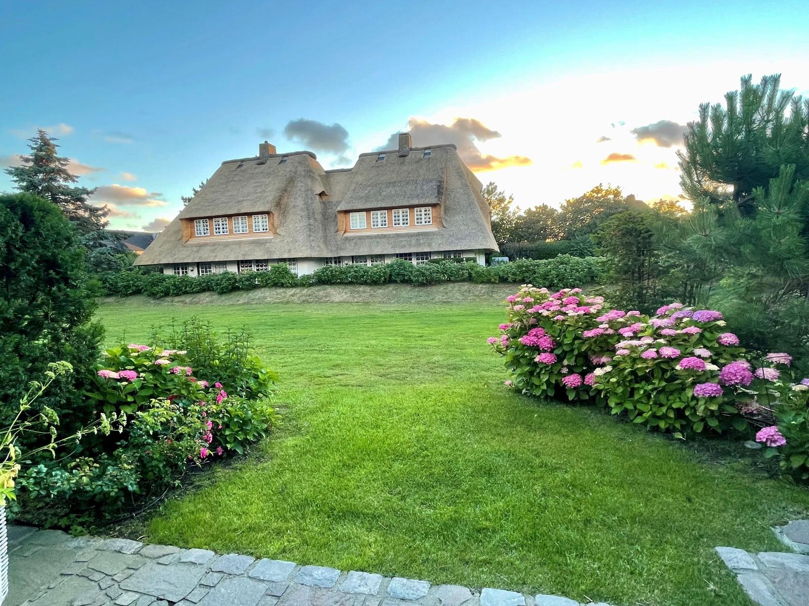 Haus mit Strohdach, grüner Rasen und blühende Hortensien im Vorgarten.