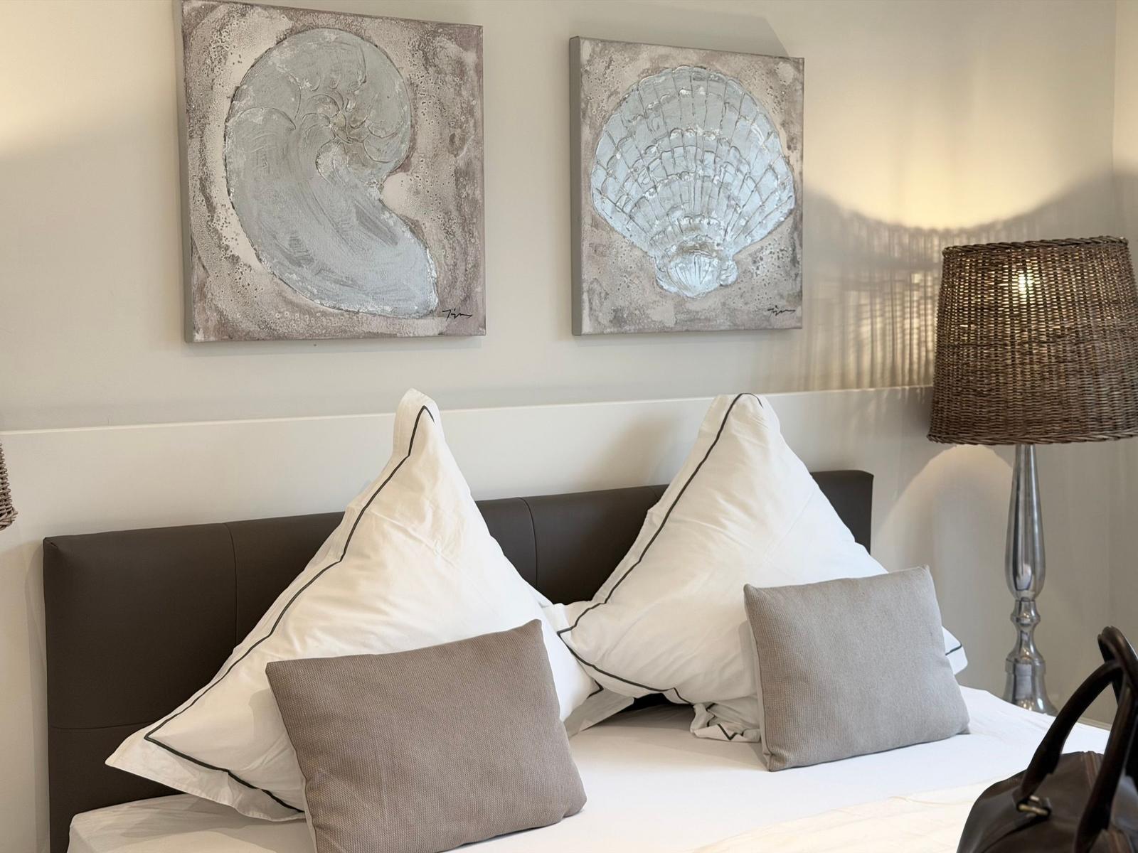 Doppelbett mit Kissen, Wandbilder von Muscheln und einer Lampe.