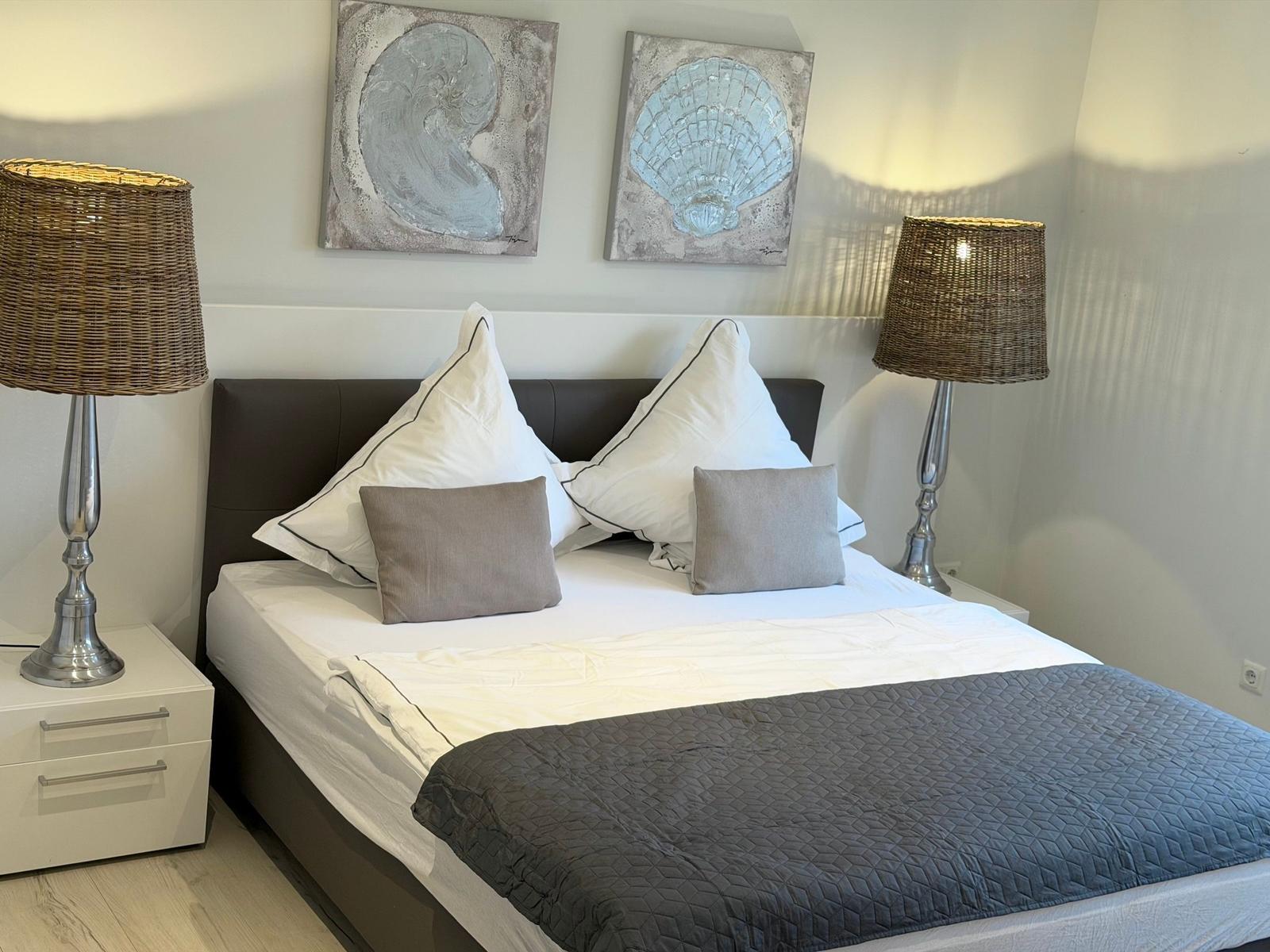 Schlafzimmer mit Bett, zwei Nachttischen und Wandbildern mit Muscheln.