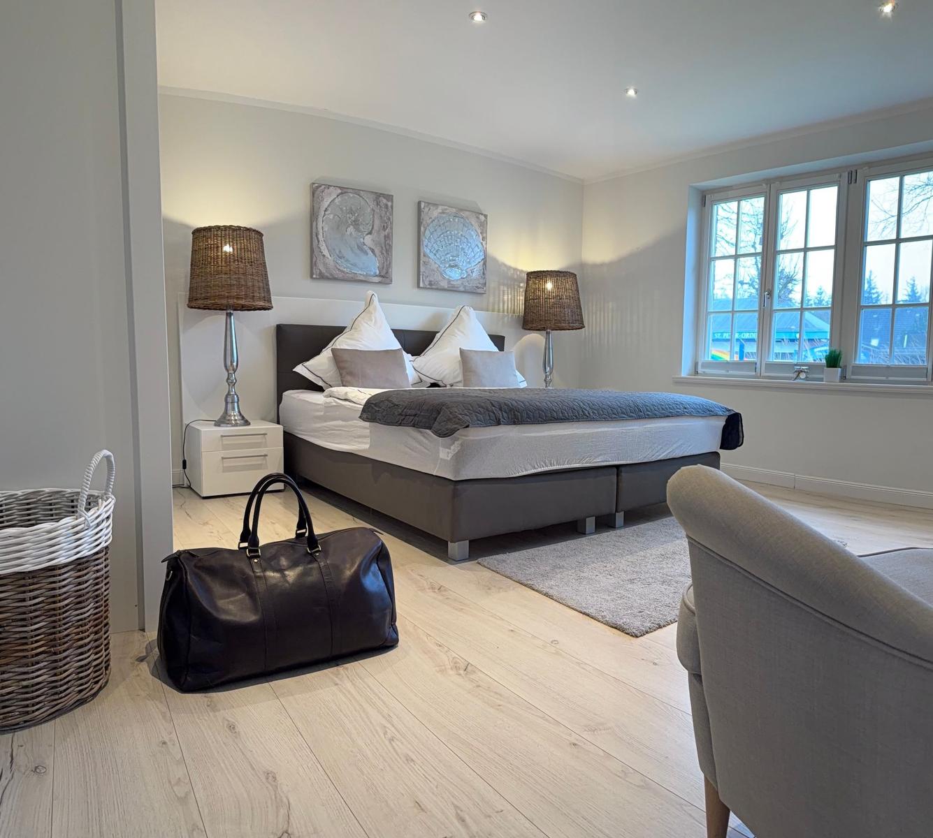 Schlafzimmer mit Bett, Nachttischen und Fenster. Auf dem Boden steht eine Tasche.