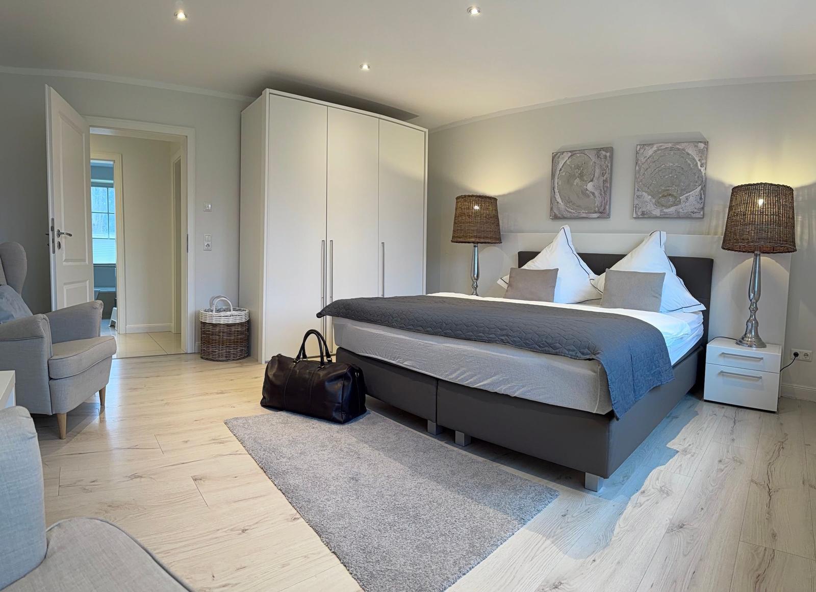Schlafzimmer mit Bett, Nachttischen und Kleiderschrank. Holzboden und Wandbilder sichtbar.