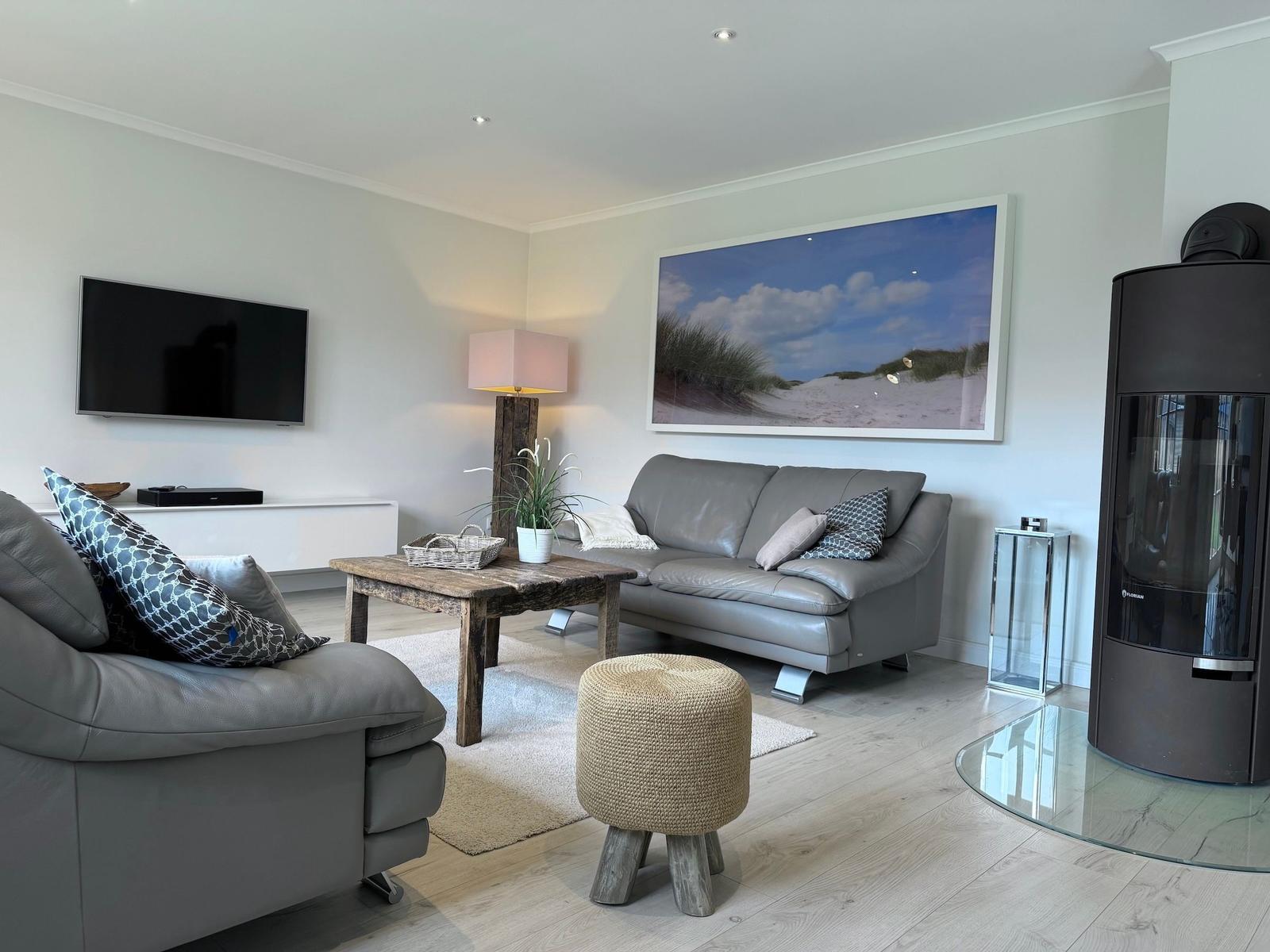 Wohnzimmer mit grauem Sofa, Holztisch und Fernseher an der Wand.