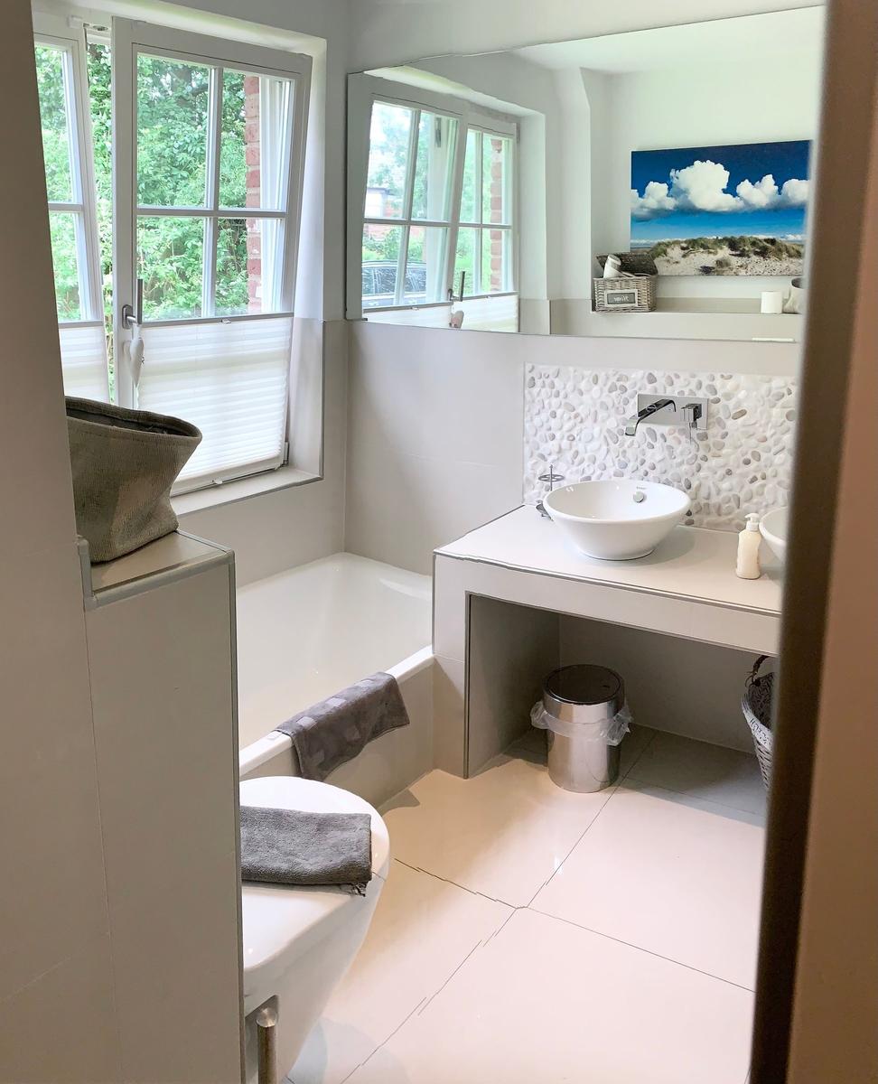 Badezimmer mit Badewanne, Waschtisch und Fenster mit Blick auf Grün.