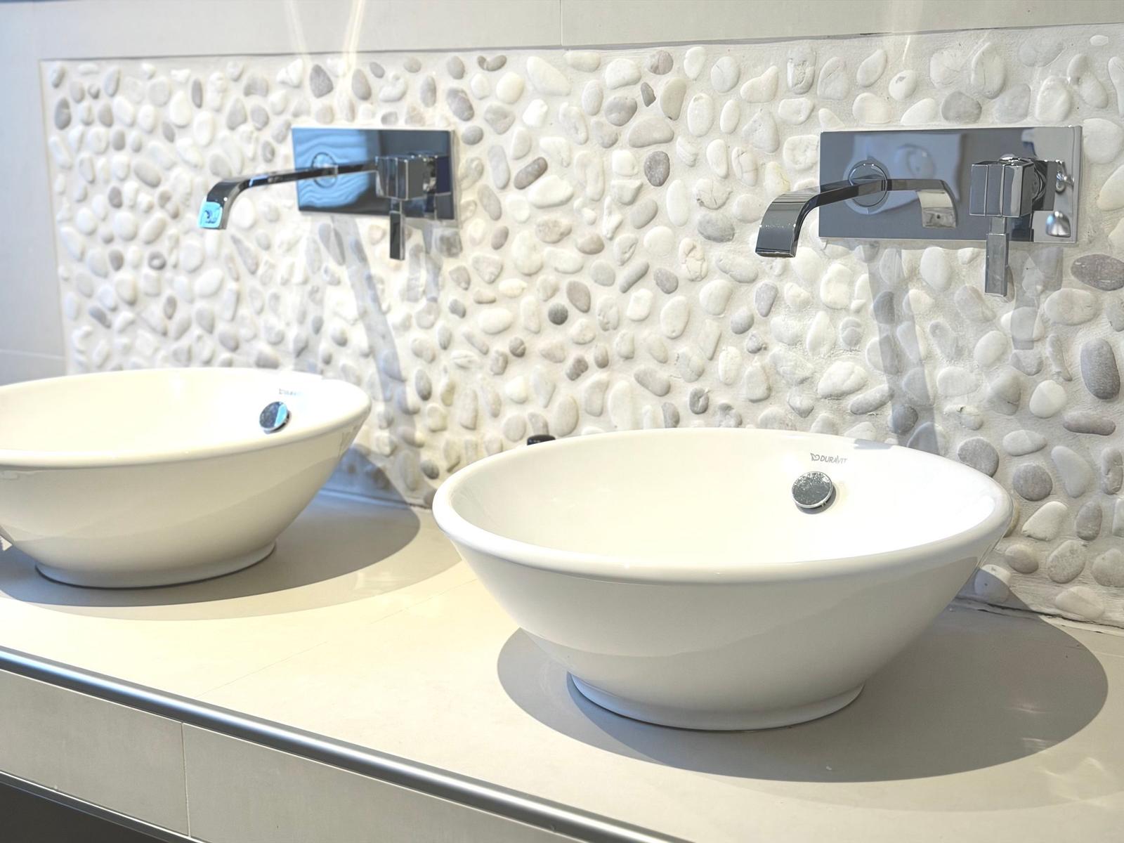 Zwei weiße Waschbecken mit modernen Wasserhähnen an einer Steinwand.