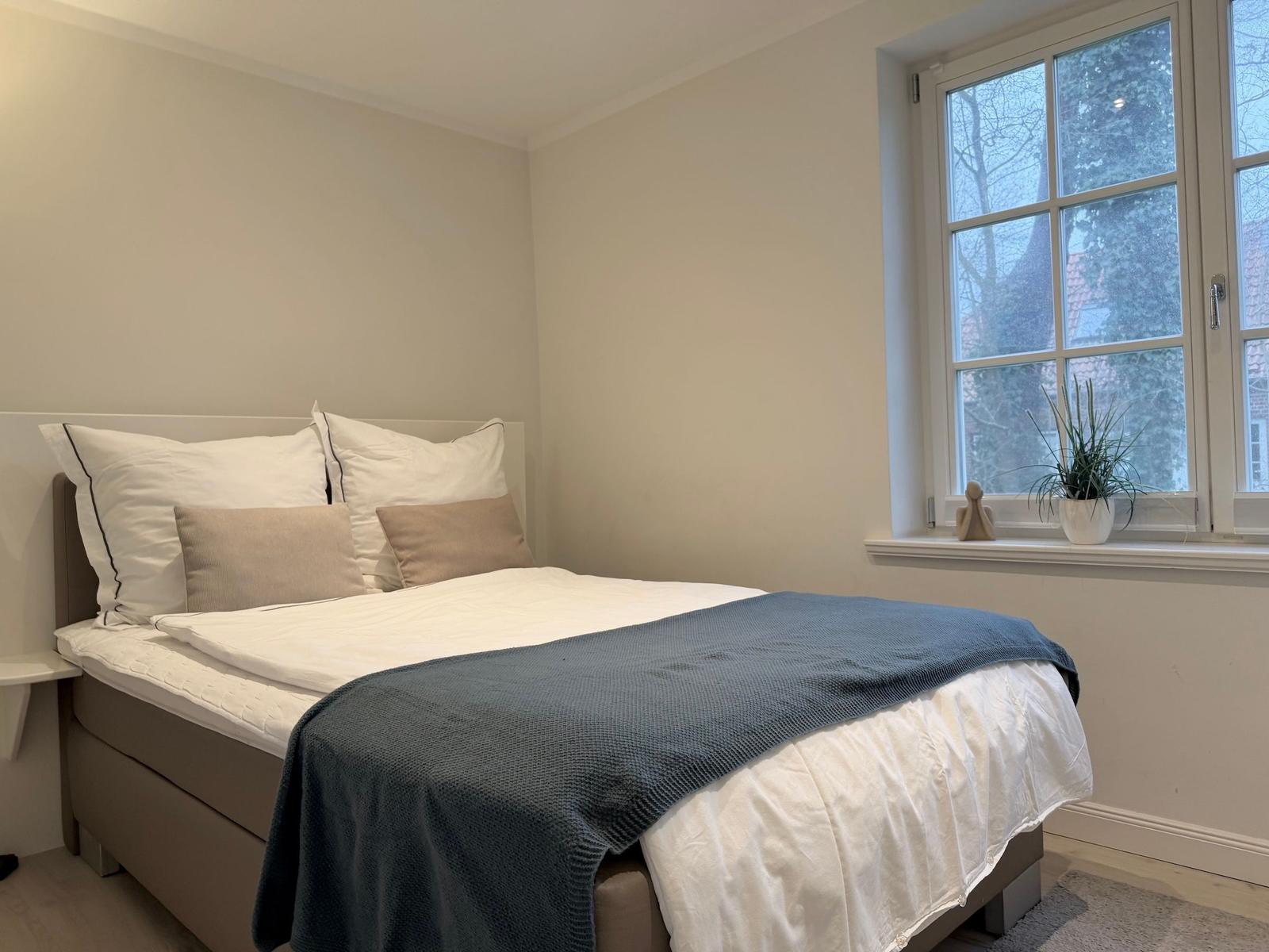 Ein Schlafzimmer mit einem Bett, Kissen und einem Fenster mit Pflanze.