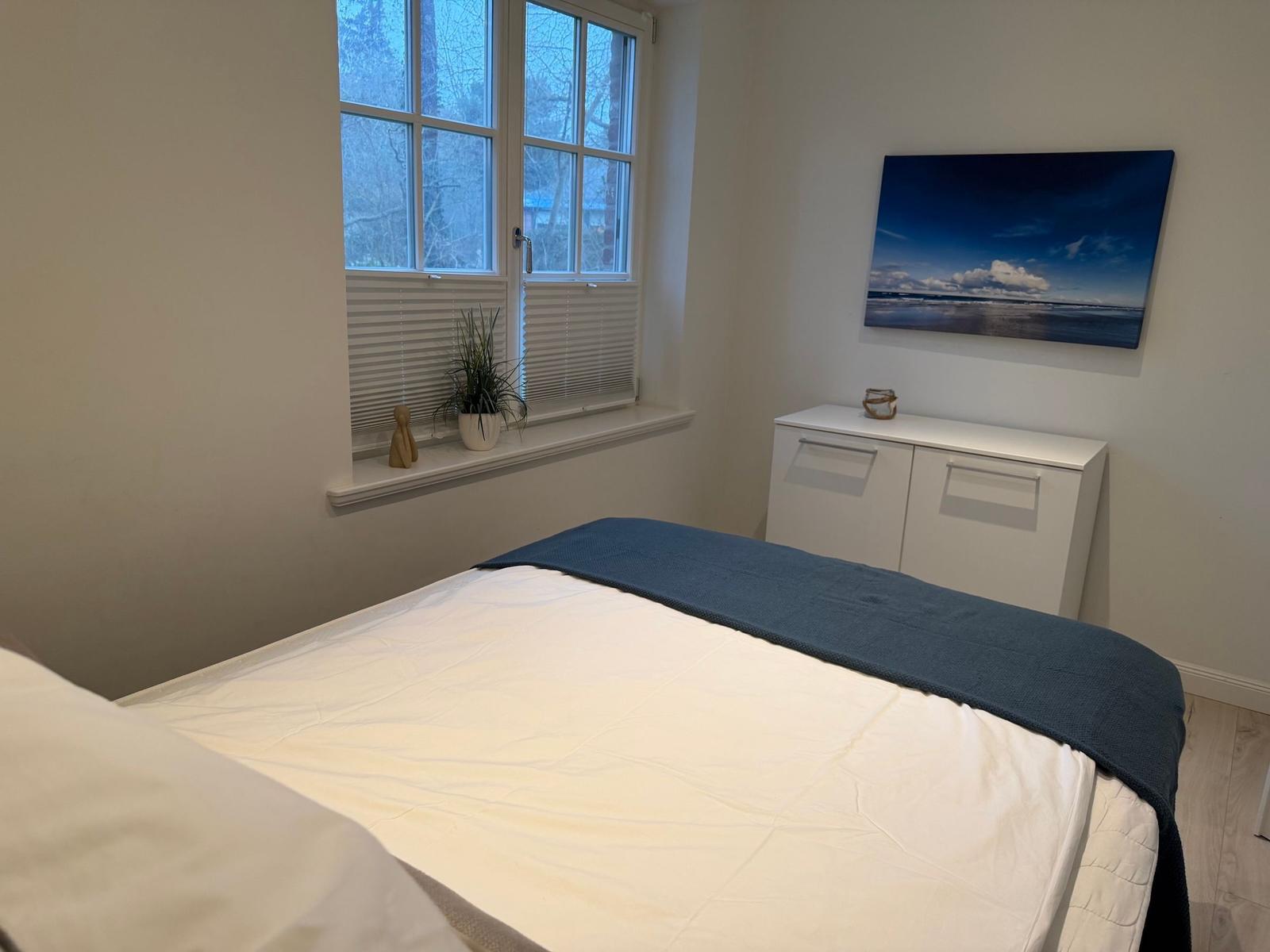 Schlafzimmer mit Bett, Fenster und Wandbild.