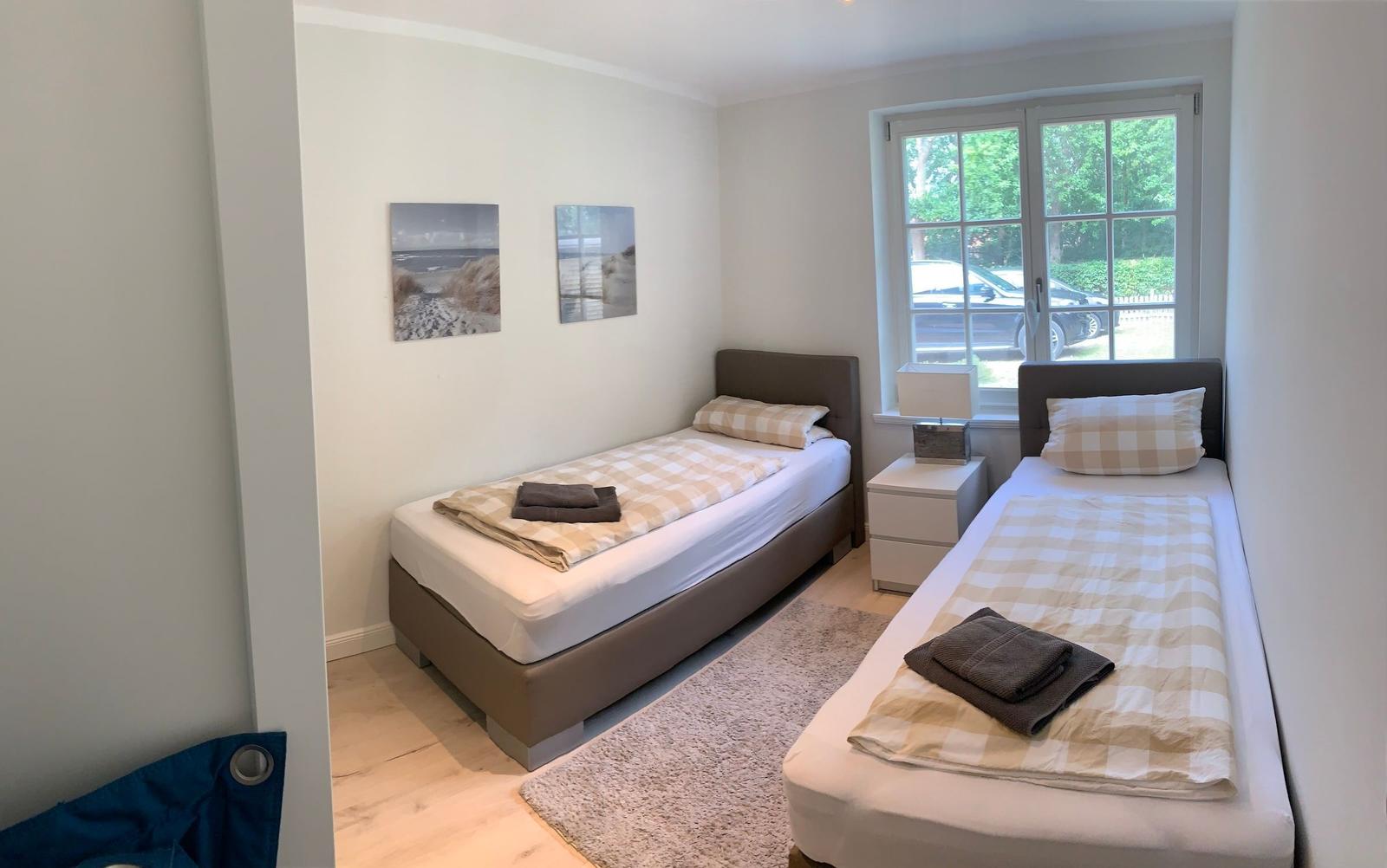 Zwei Einzelbetten mit Kissen und Decken, Fenster mit Blick nach draußen, Wandbilder und Nachttisch.