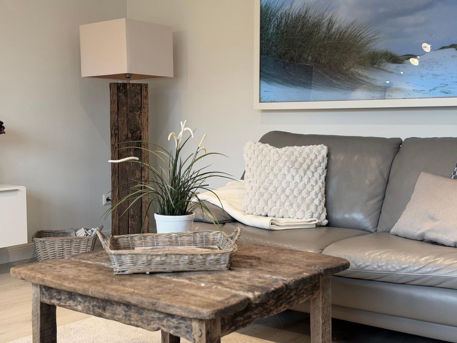 Ein grauer Sofa mit Kissen, Holztisch und Wandbild mit Strandmotiv.