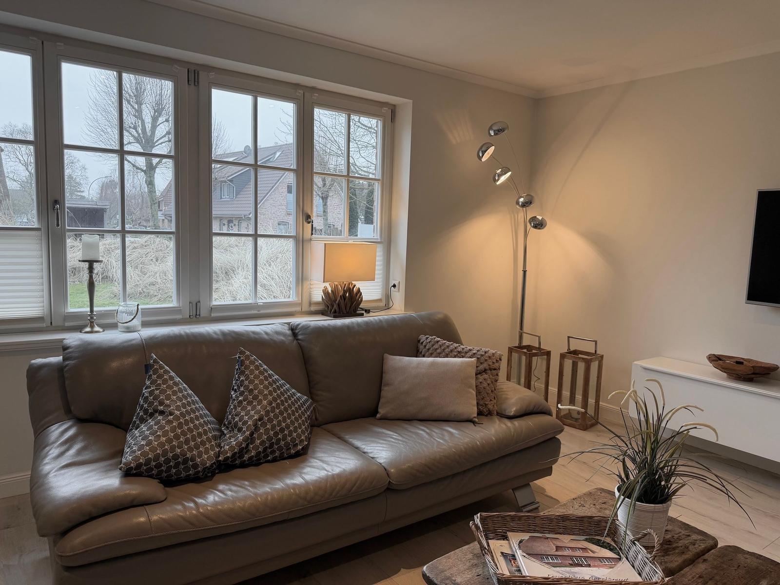 Ein Wohnzimmer mit braunem Sofa, Fenstern und Stehlampe.