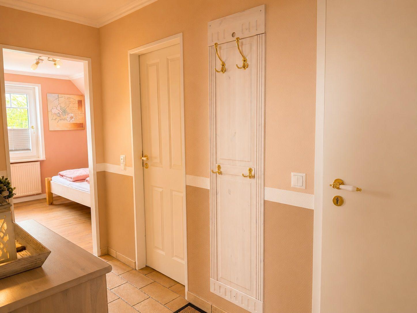 Flur mit Garderobe, Tür und Blick in Schlafzimmer mit Bett und Fenster.
