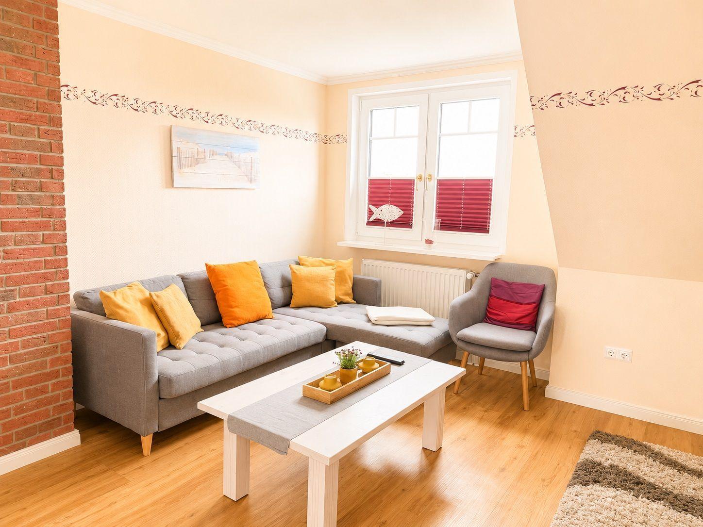 Wohnzimmer mit grauem Sofa, orangefarbenen Kissen und Holzboden.