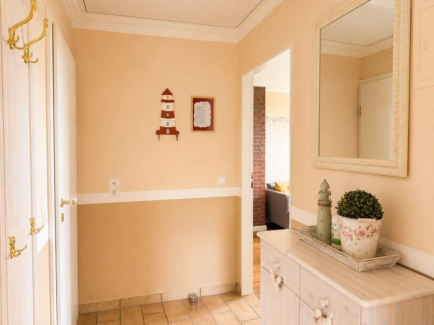 Flur mit Garderobe, Spiegel und Dekoration. Durchgang zu Wohnzimmer mit Sofa.
