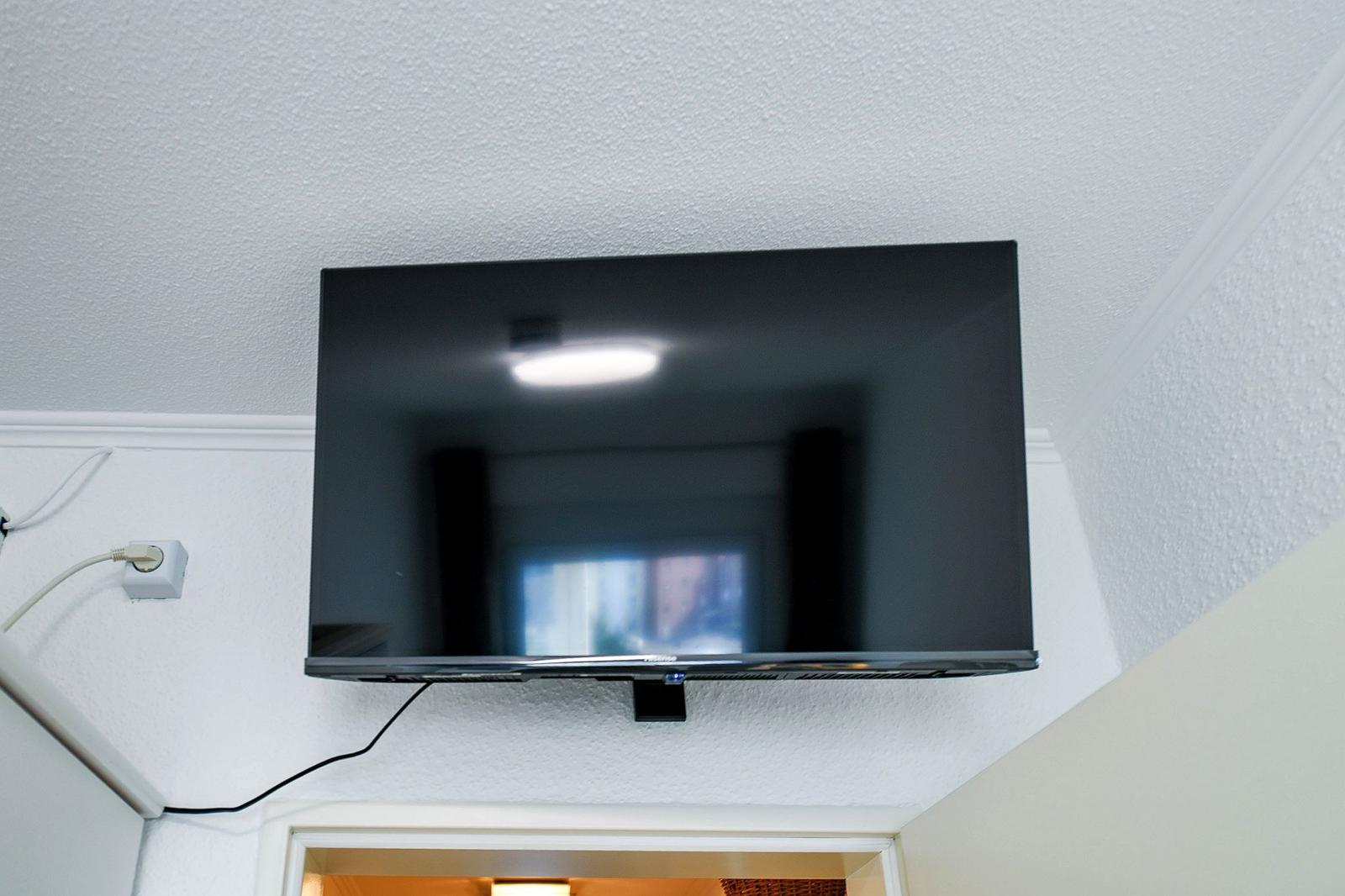 Flachbildfernseher an der Decke montiert, Kabel sind sichtbar.