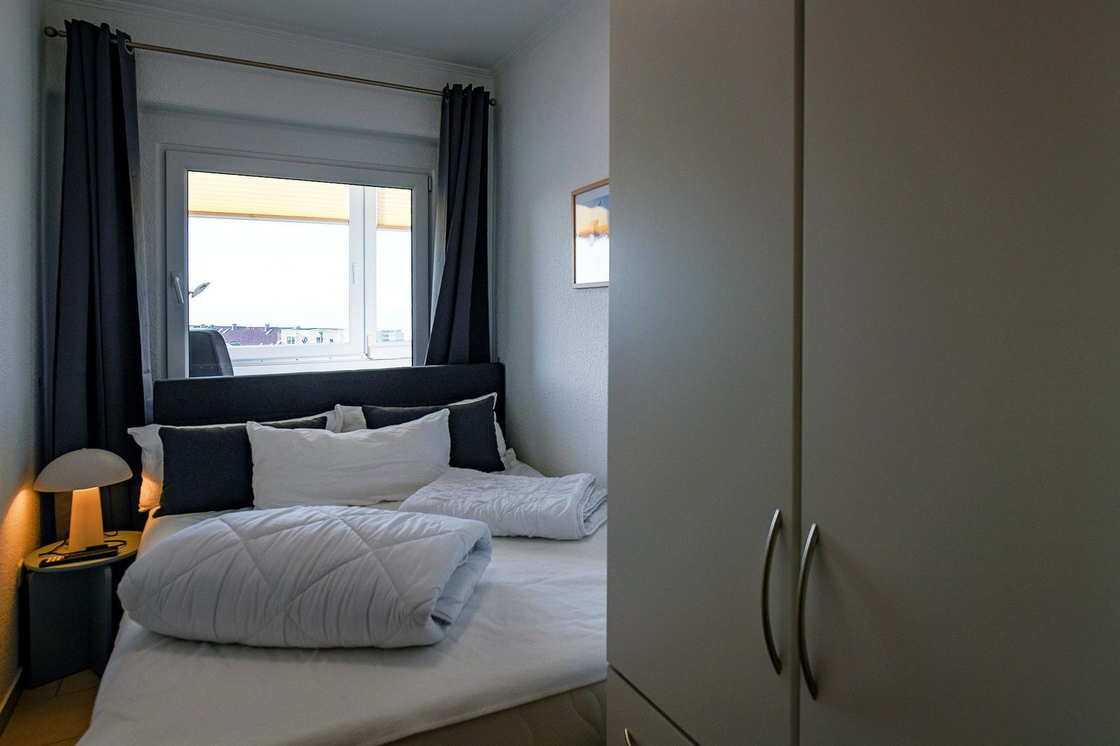Schlafzimmer mit Bett, Fenster und Kleiderschrank.