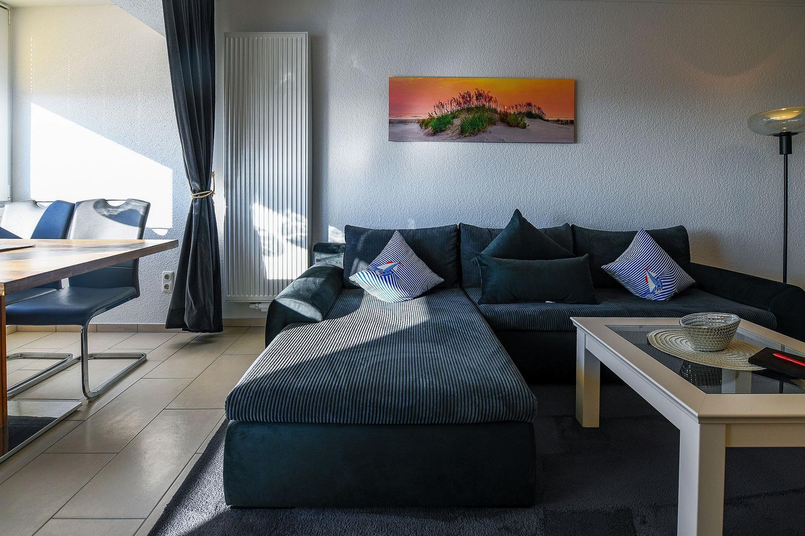 Ein Wohnzimmer mit Sofa, Couchtisch und Wandbild. Links ein Esstisch mit Stühlen.