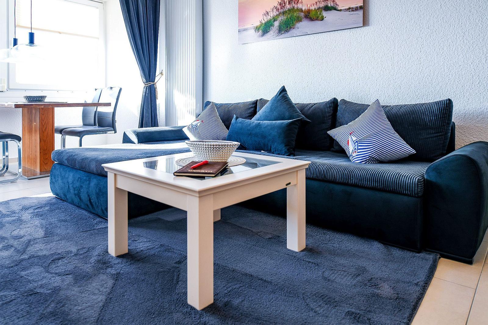 Ein Wohnzimmer mit blauem Sofa, Glas-Tisch und Wandbild.