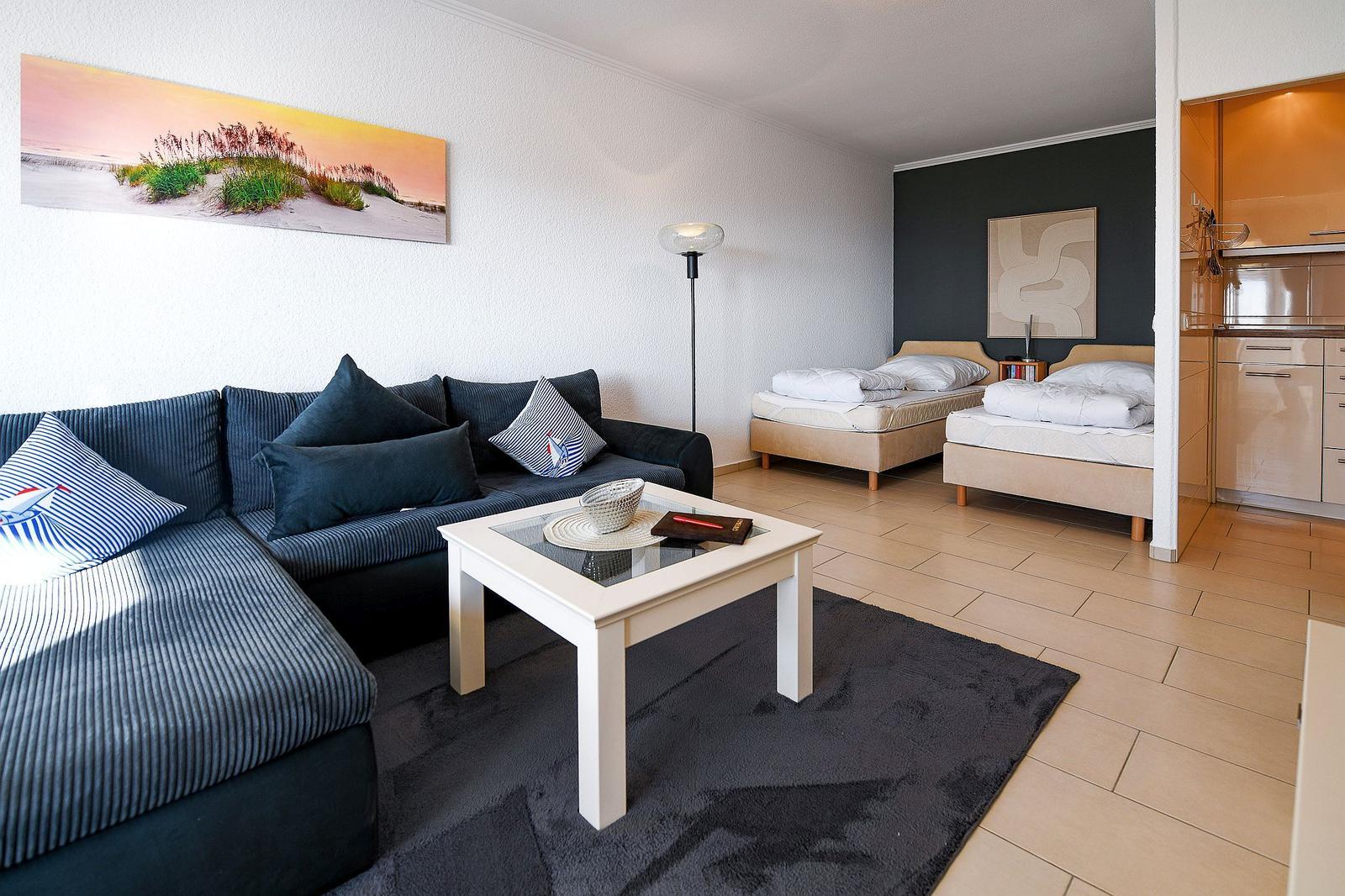 Wohnbereich mit Sofa, Tisch und zwei Betten im Hintergrund.