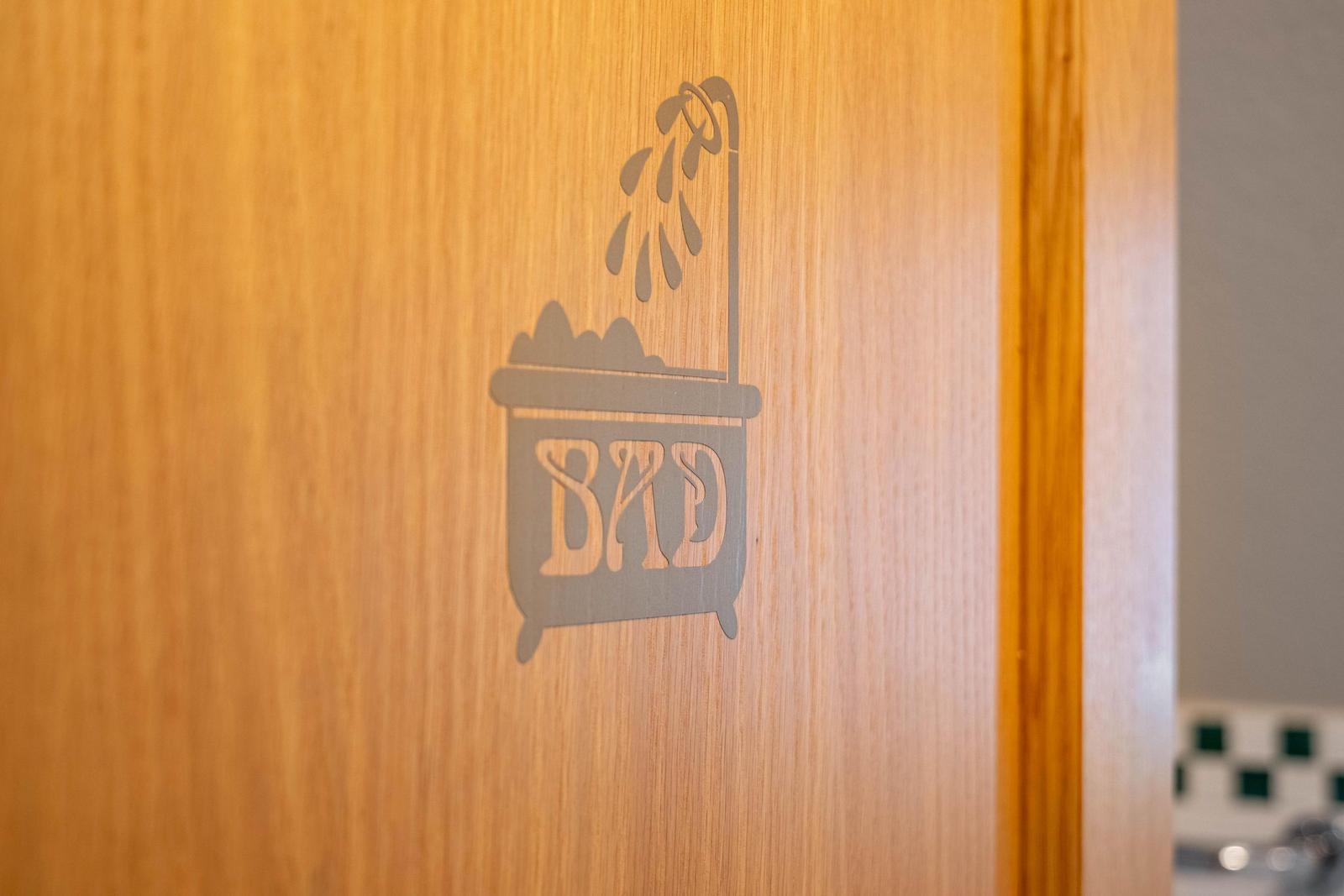 Holztür mit eingraviertem Bad-Symbol und Duschkopf