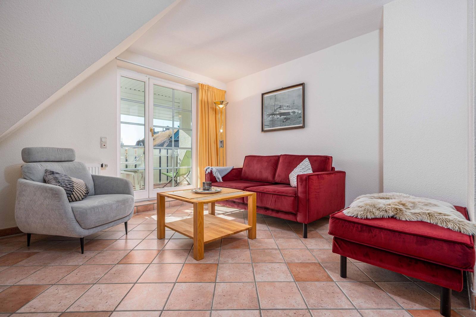 Wohnzimmer mit rotem Sofa, grauer Sessel und Terrasse. Holztisch und Wandbild.