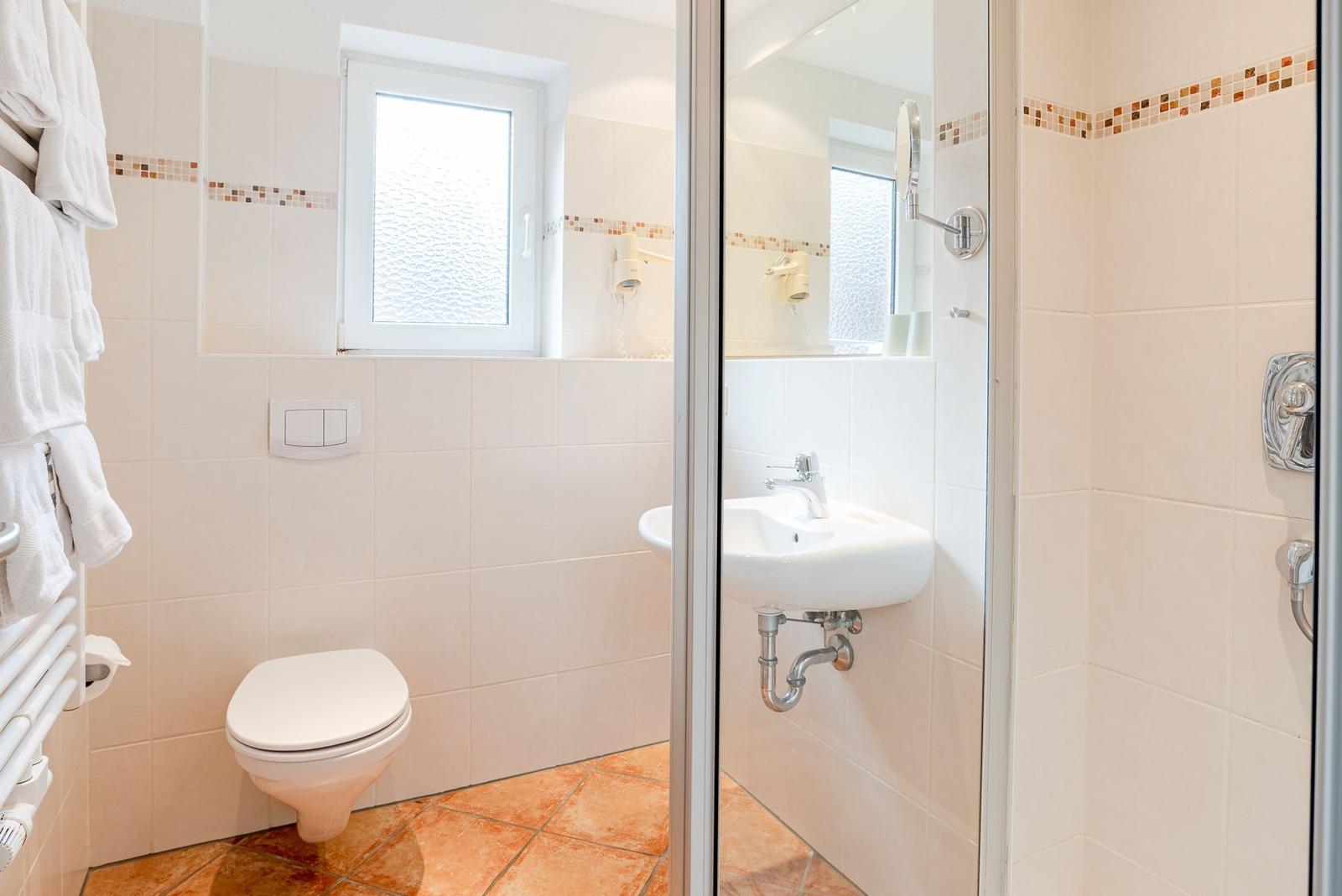 Badezimmer mit Toilette, Waschbecken und Dusche. Fenster mit Milchglas.