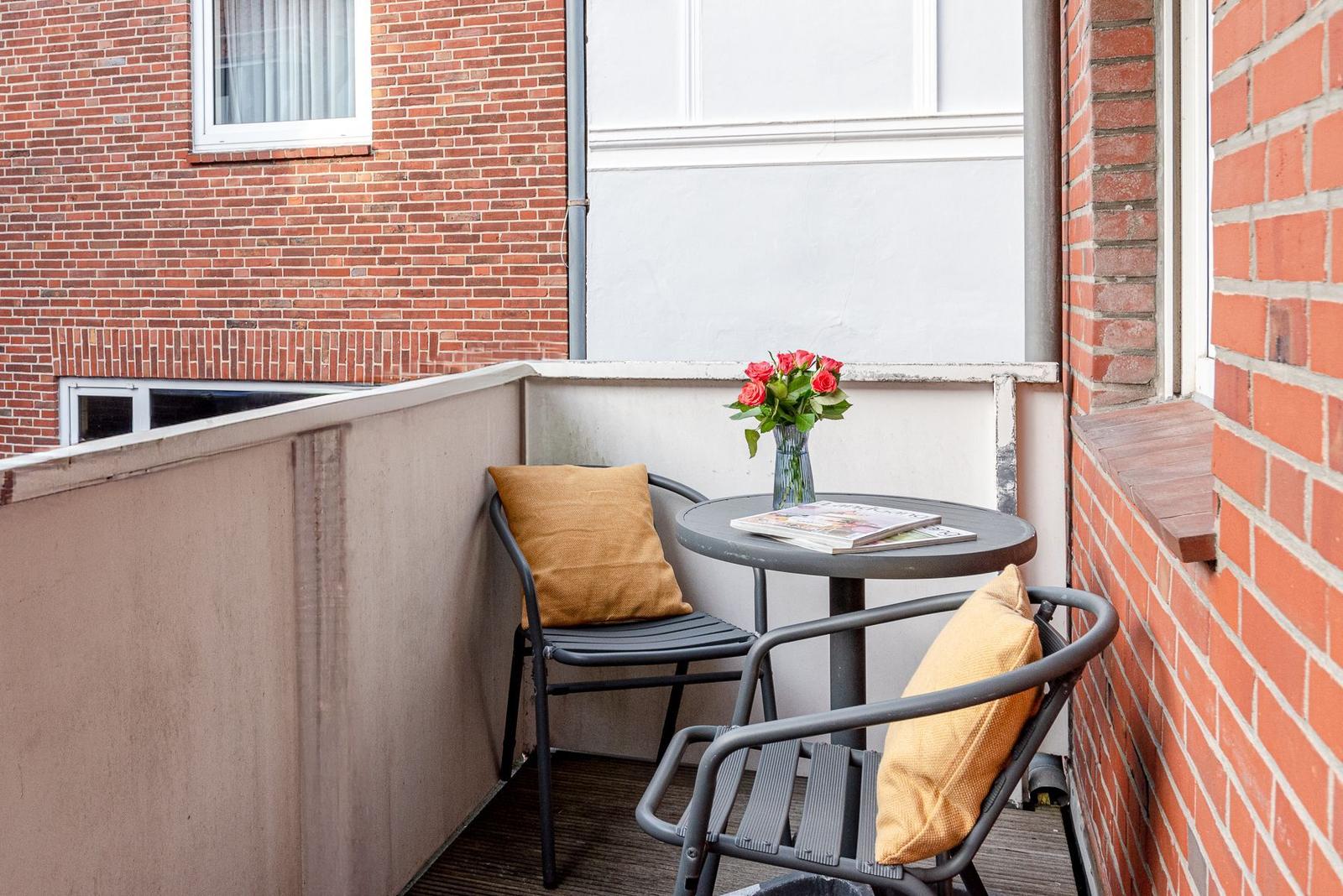 Ein kleiner Balkon mit zwei Stühlen, einem Tisch und einer Vase mit Rosen.