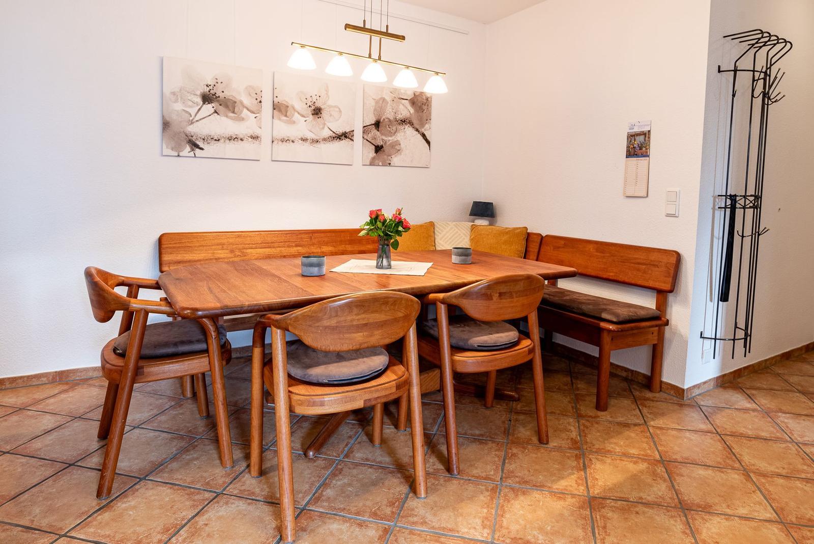 Essbereich mit Holztisch, Stühlen und Bänken. Wandbild mit Blumenmotiv und hängende Lampe.