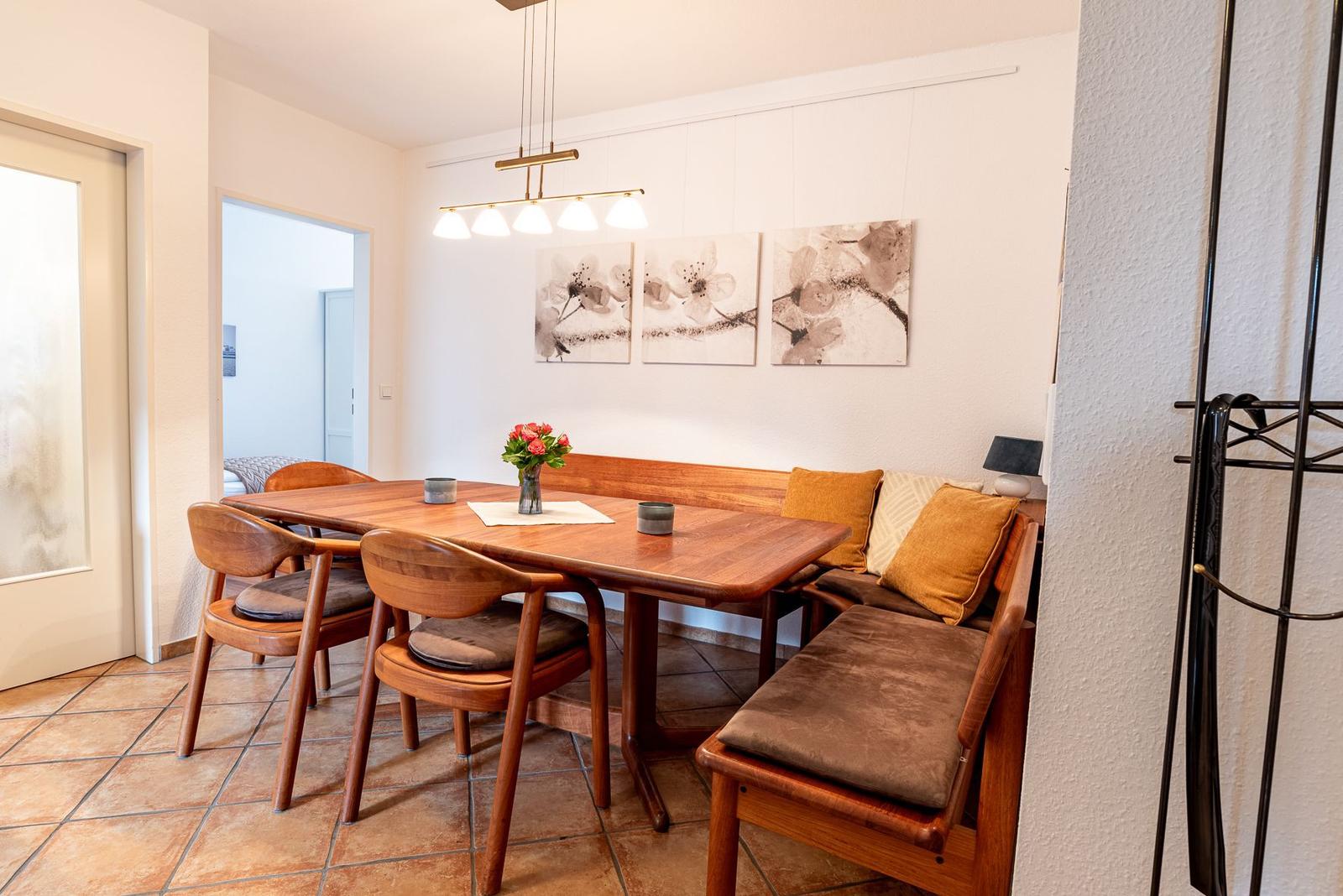 Essbereich mit Holztisch, Sitzbank und Stühlen. Wandbild und Deckenleuchte sichtbar.