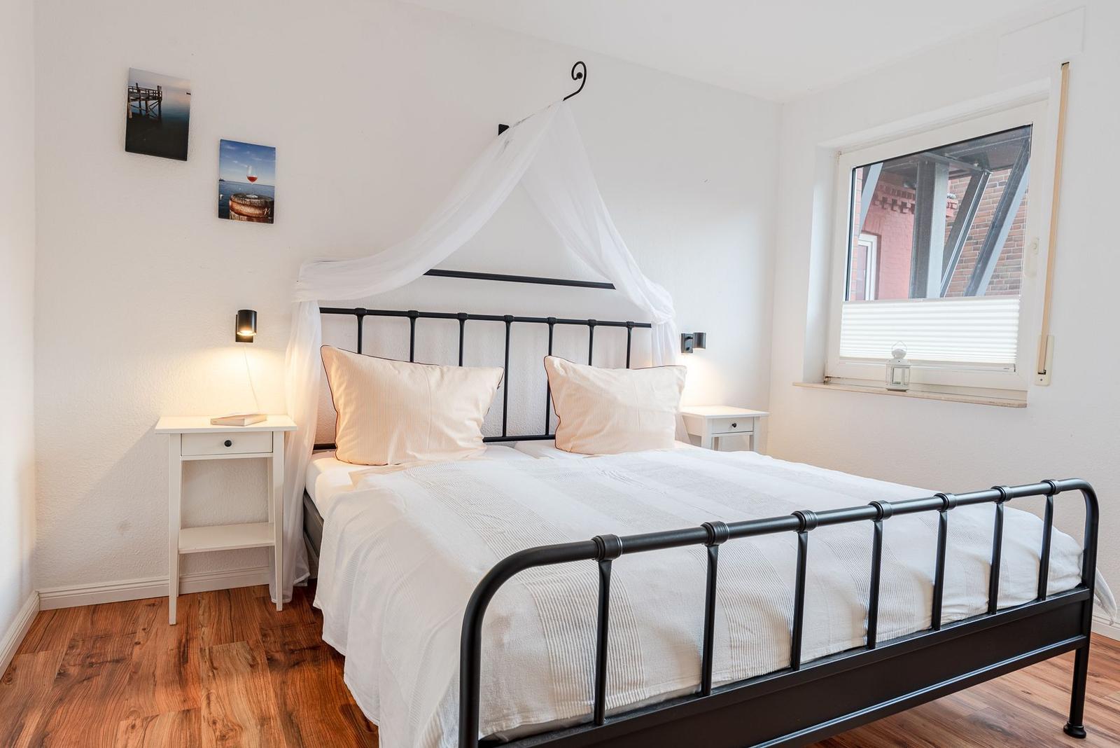 Schlafzimmer mit schwarzem Metallbett, weißen Vorhängen und Holzboden.